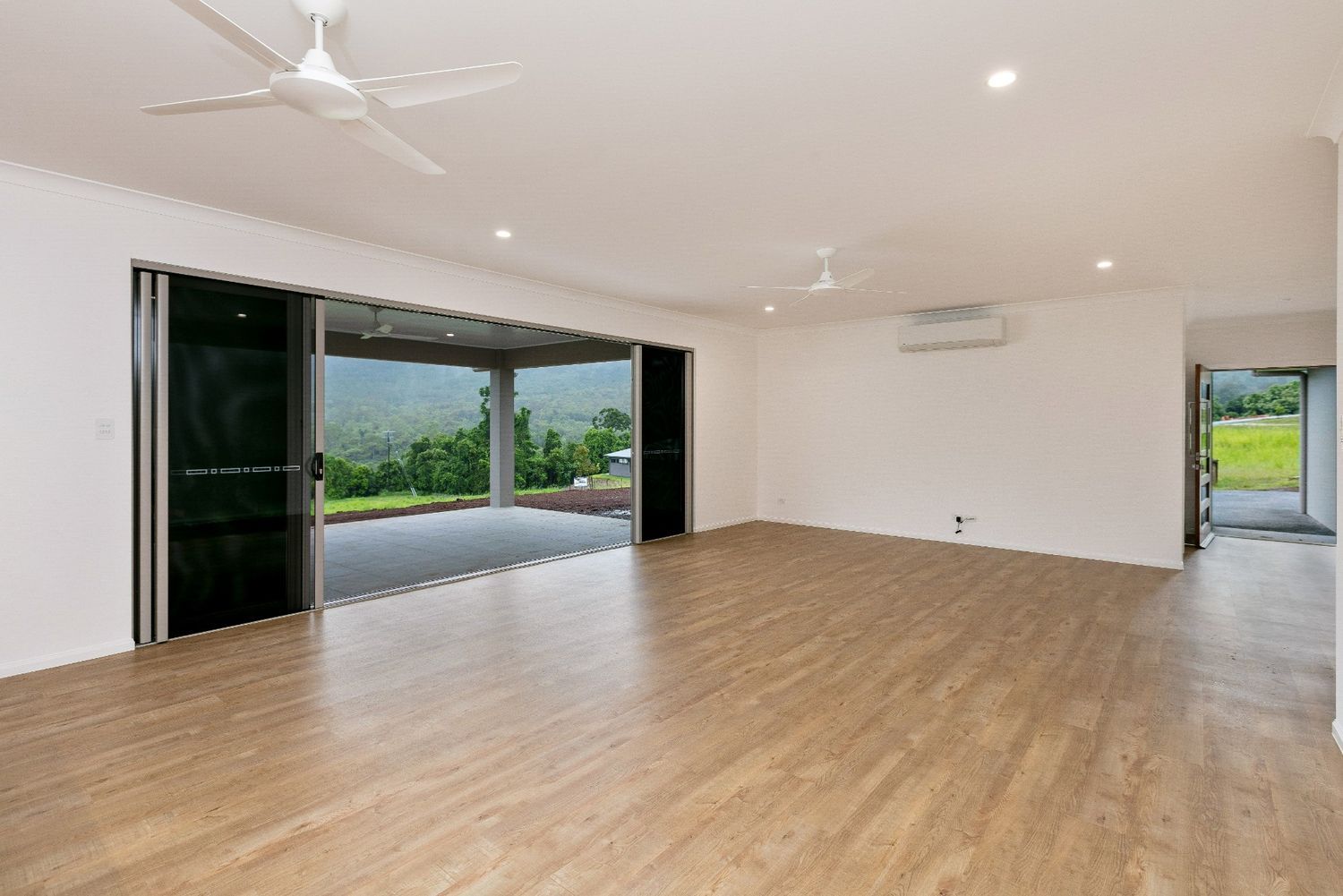 A Large Empty Room With Wooden Floors and a Ceiling Fan — Ashlee Jones Homes in Gordonvale, QLD