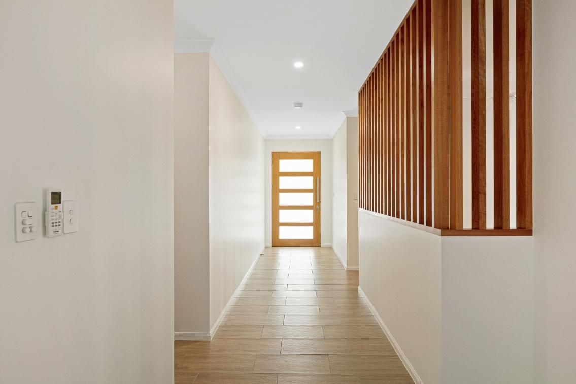 A Long Hallway in a House With a Wooden Door and a Wooden Divider — Ashlee Jones Homes in Gordonvale, QLD