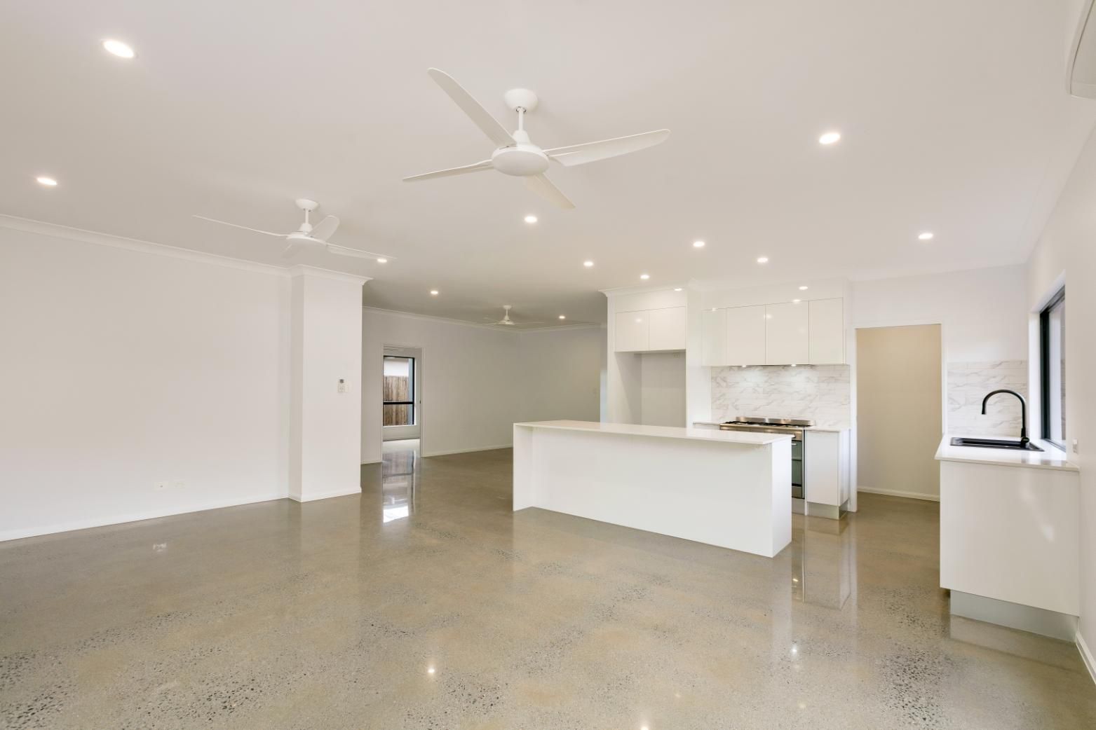 A Large Empty Room With a Ceiling Fan and a Kitchen — Ashlee Jones Homes in Gordonvale, QLD
