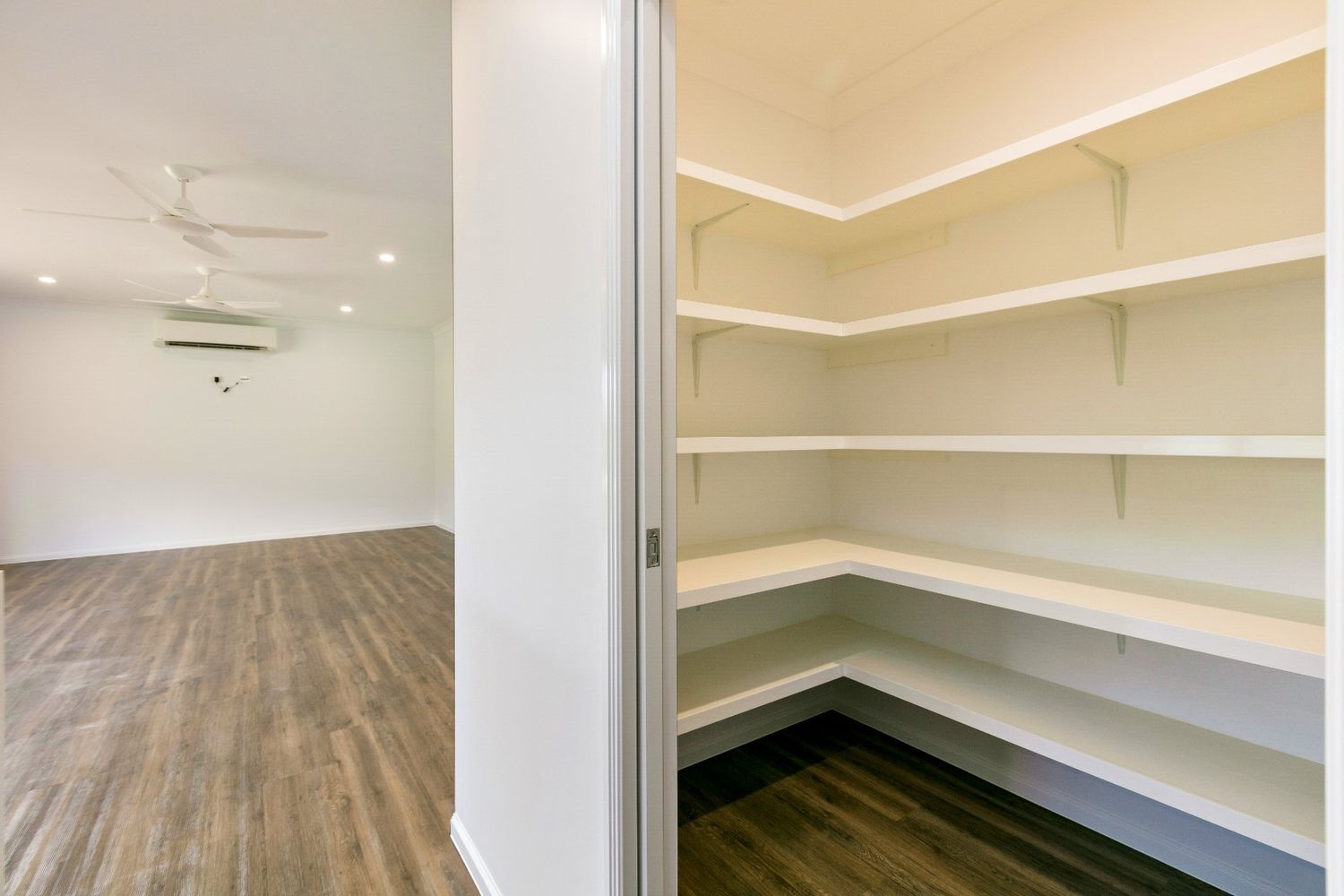 An Empty Room With Hardwood Floors and White Shelves — Ashlee Jones Homes in Gordonvale, QLD