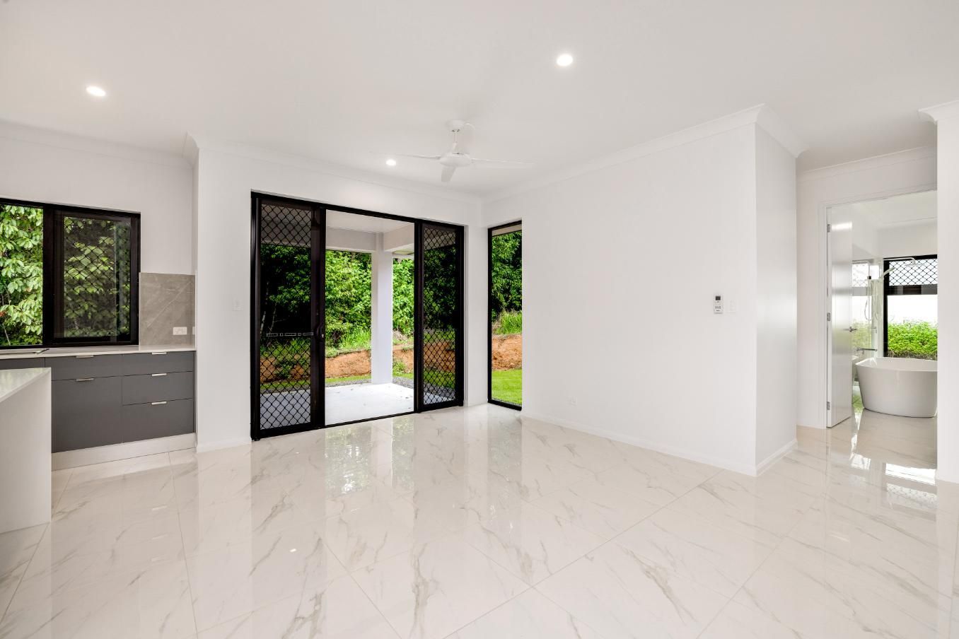 An Empty Living Room With Marble Floors and Sliding Glass Doors Leading to a Bathroom — Ashlee Jones Homes in Gordonvale, QLD