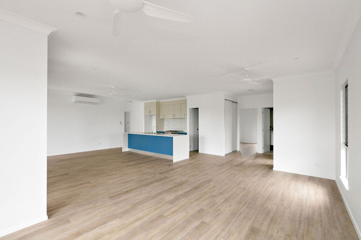 A Large Empty Room With Hardwood Floors and White Walls — Ashlee Jones Homes in Gordonvale, QLD