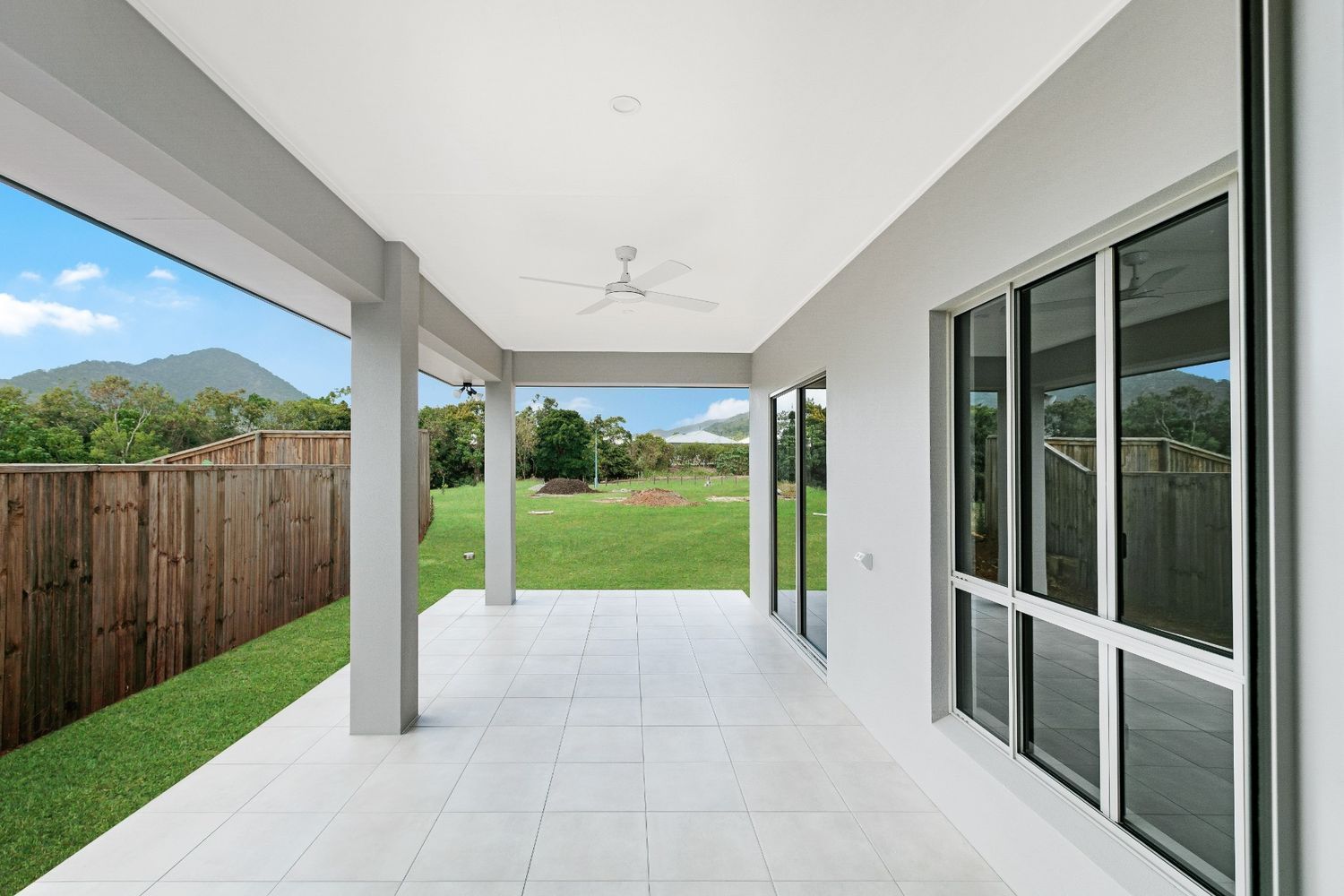 An Empty Patio With a Ceiling Fan and Sliding Glass Doors Leading to a Backyard — Ashlee Jones Homes in Gordonvale, QLD
