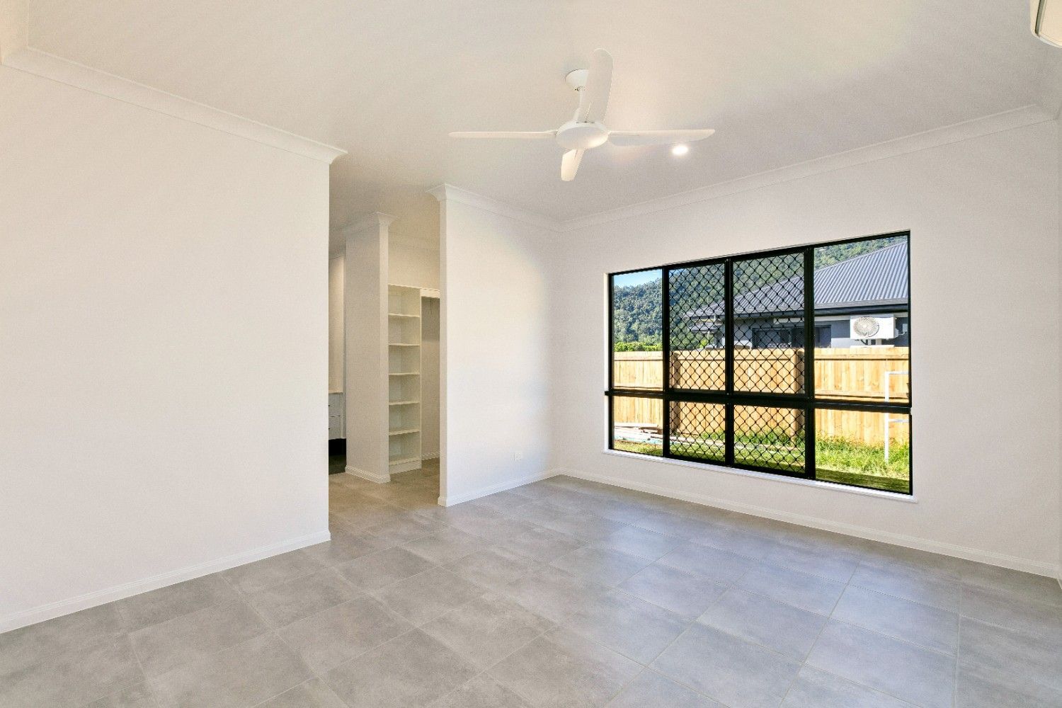An Empty Living Room With a Ceiling Fan and a Large Window  — Ashlee Jones Homes in Gordonvale, QLD