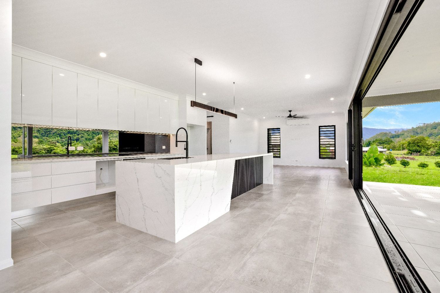 A Kitchen With a Large Island and Sliding Glass Doors Leading to a Patio — Ashlee Jones Homes in Gordonvale, QLD