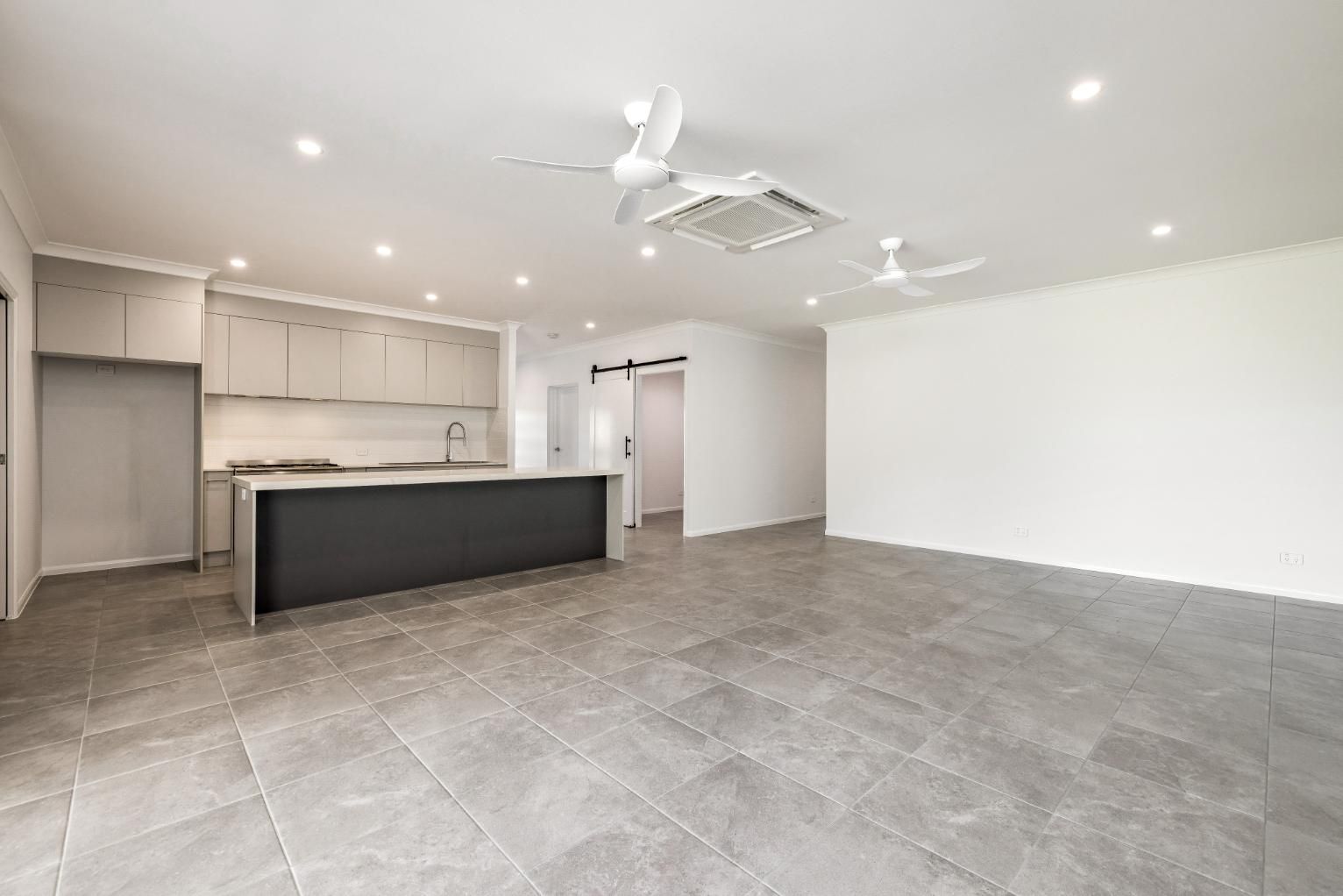 An Empty Living Room With a Kitchen and a Ceiling Fan — Ashlee Jones Homes in Gordonvale, QLD