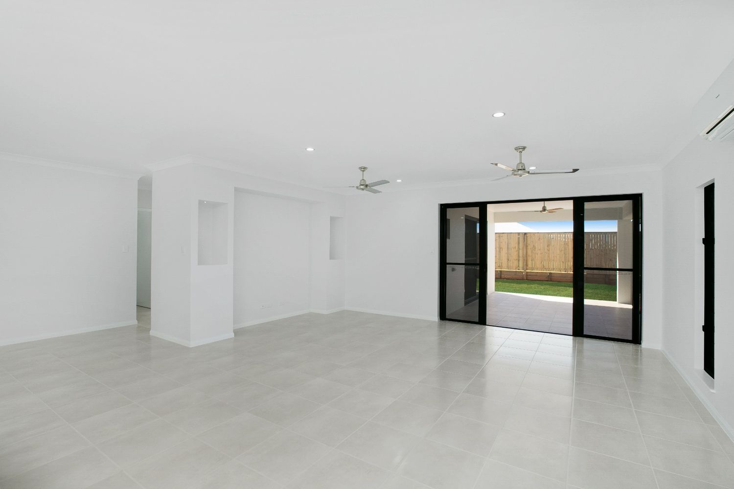 An Empty Living Room With a Ceiling Fan and Sliding Glass Doors — Ashlee Jones Homes in Gordonvale, QLD