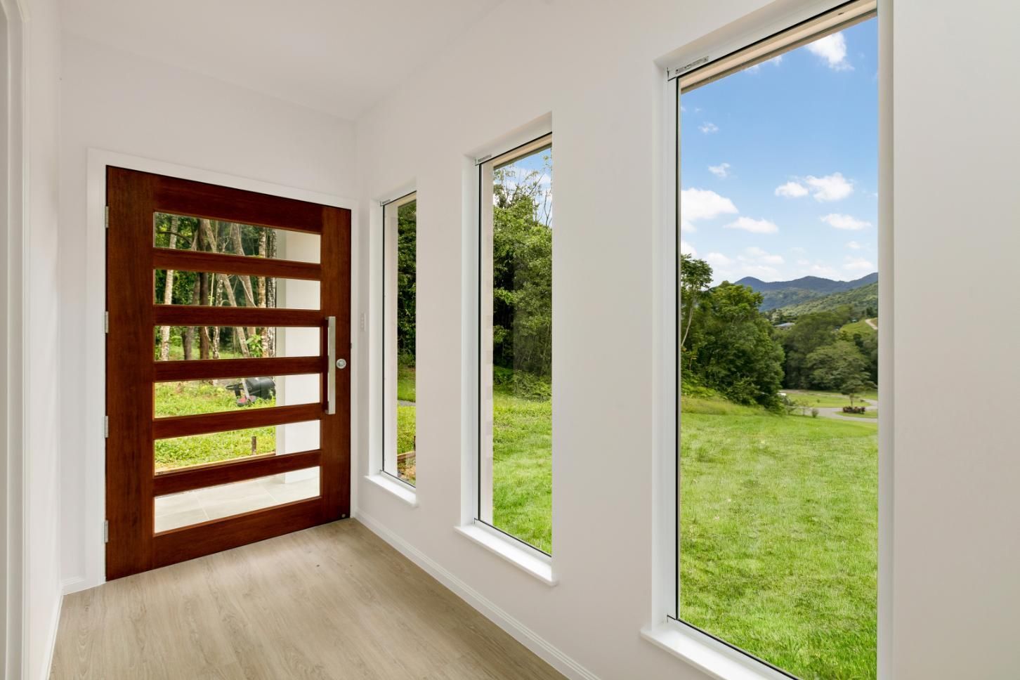 A Hallway With a Wooden Door and Three Windows With a View of a Field — Ashlee Jones Homes in Gordonvale, QLD