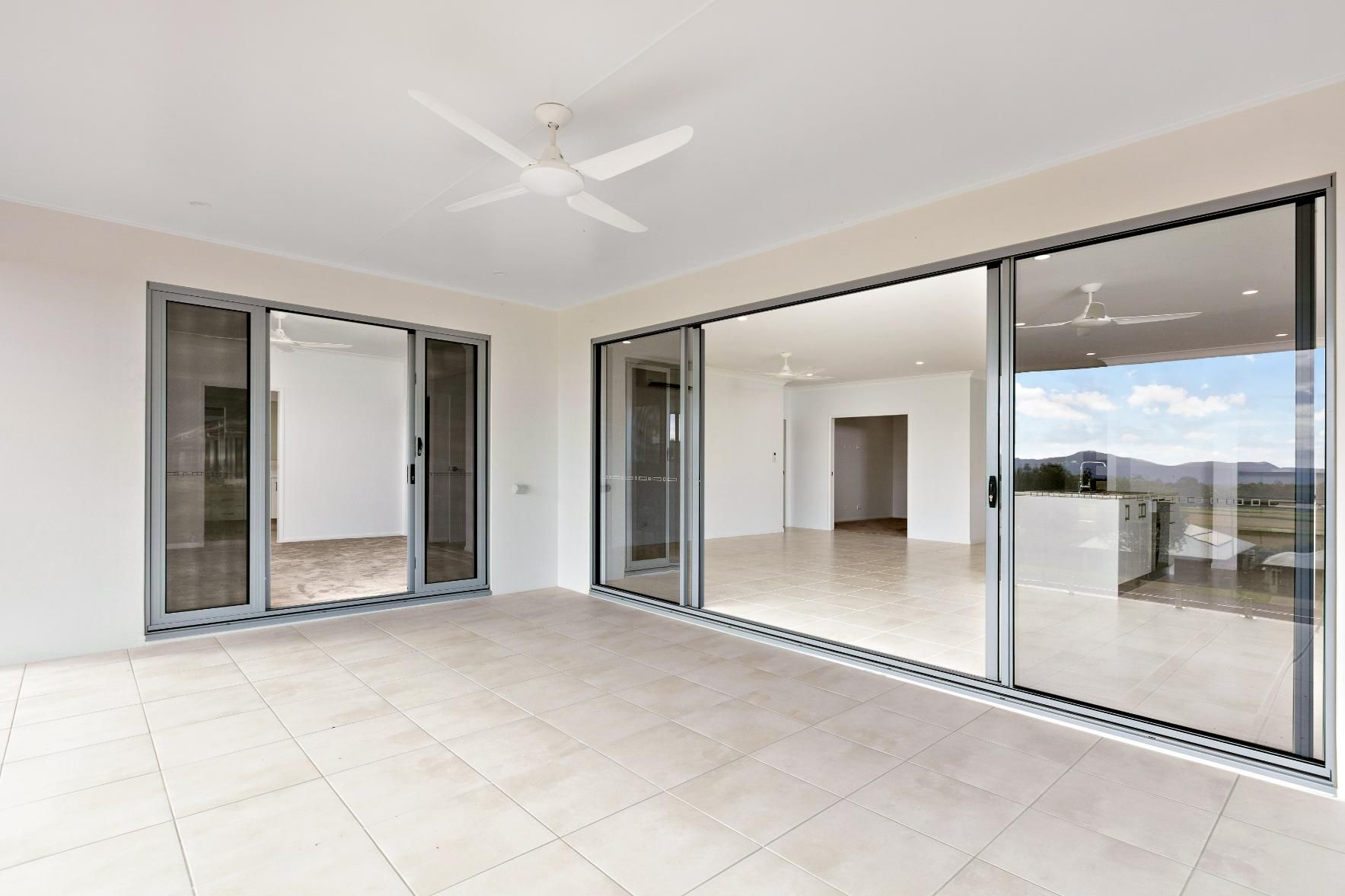 A Large Empty Room With Sliding Glass Doors and a Ceiling Fan — Ashlee Jones Homes in Gordonvale, QLD
