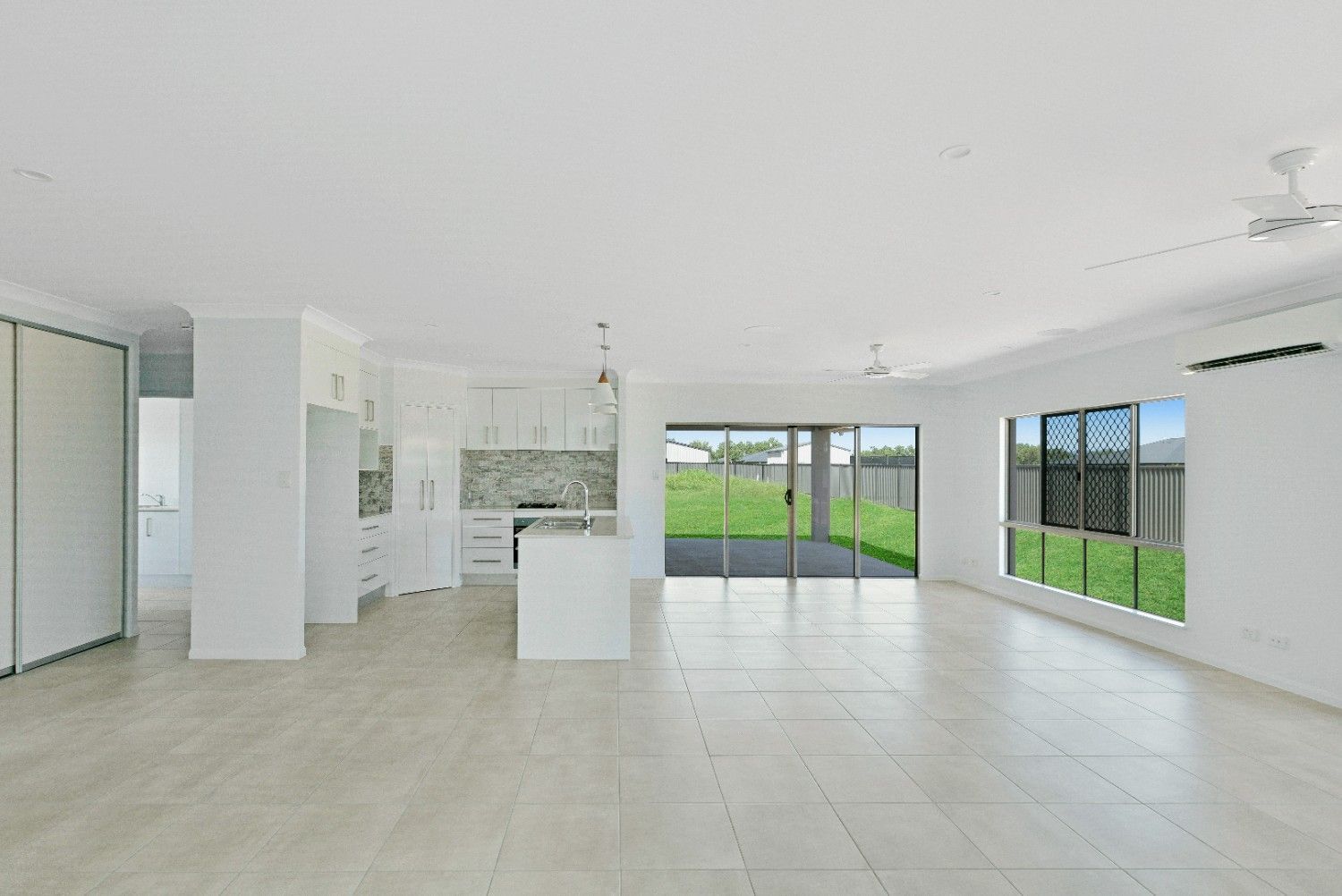 A Large Empty Room With a Kitchen and Sliding Glass Doors — Ashlee Jones Homes in Gordonvale, QLD