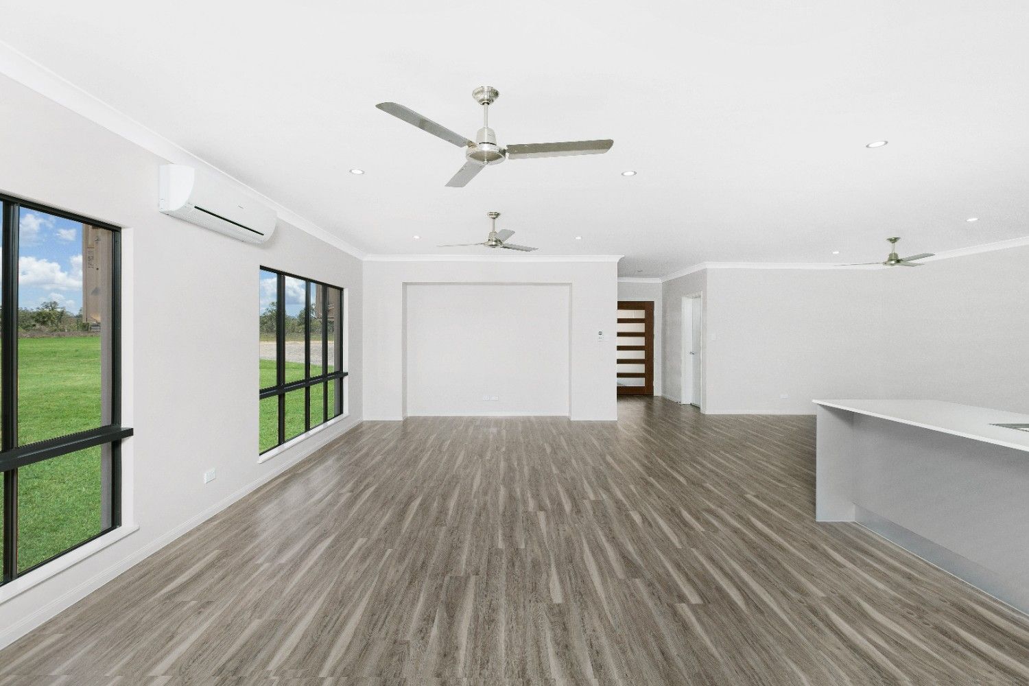An Empty Living Room With Hardwood Floors and a Ceiling Fan — Ashlee Jones Homes in Gordonvale, QLD