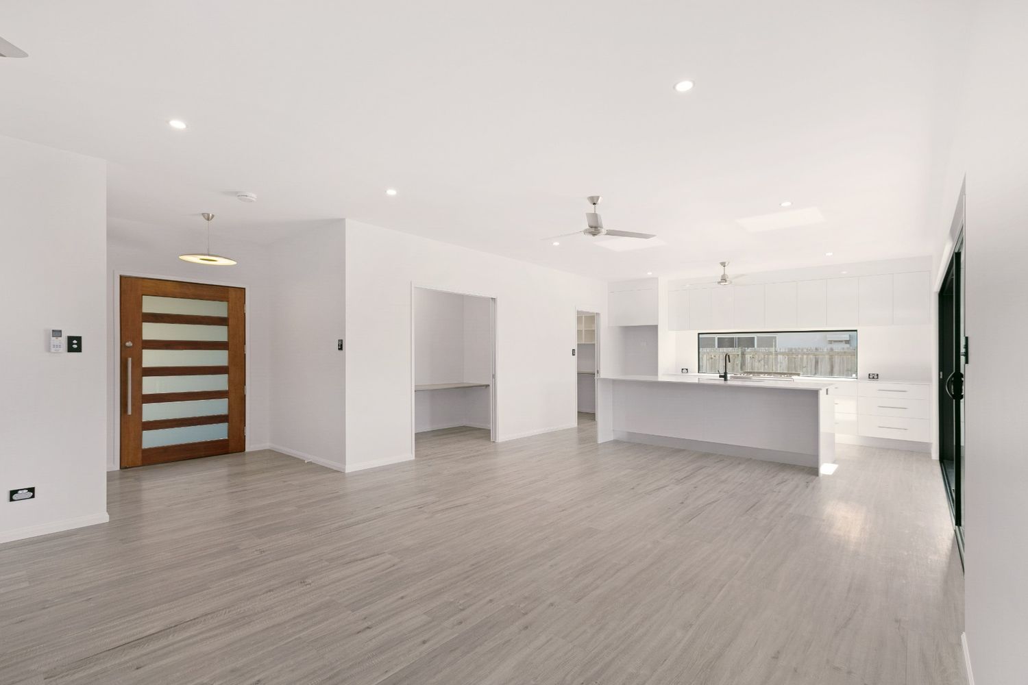 A Large Empty Room With a Wooden Floor and White Walls — Ashlee Jones Homes in Gordonvale, QLD