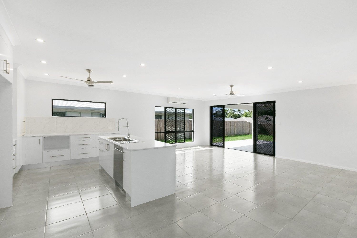An Empty Kitchen With White Cabinets and a Ceiling Fan — Ashlee Jones Homes in Gordonvale, QLD