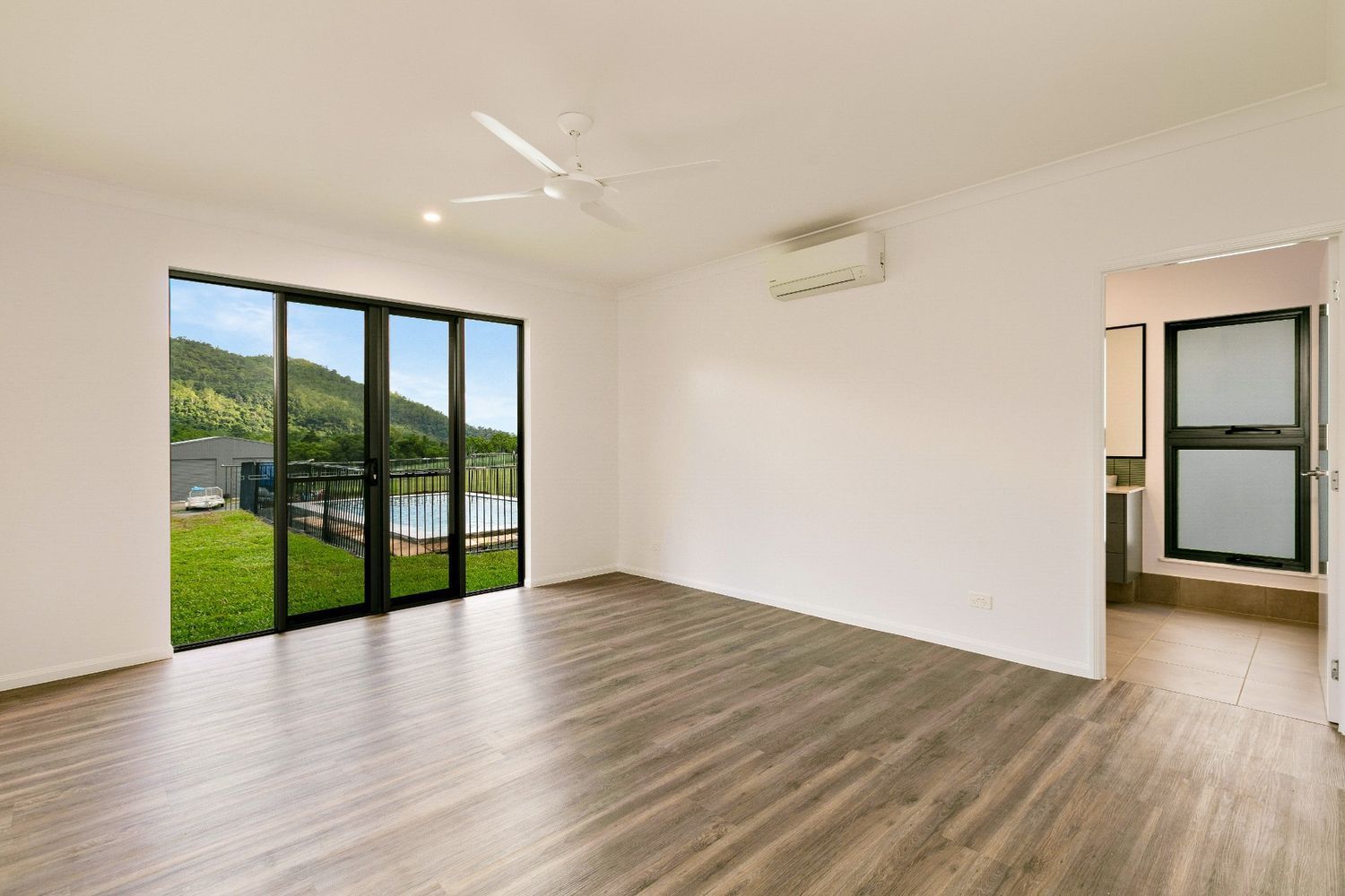 An Empty Living Room With Hardwood Floors and Sliding Glass Doors — Ashlee Jones Homes in Gordonvale, QLD