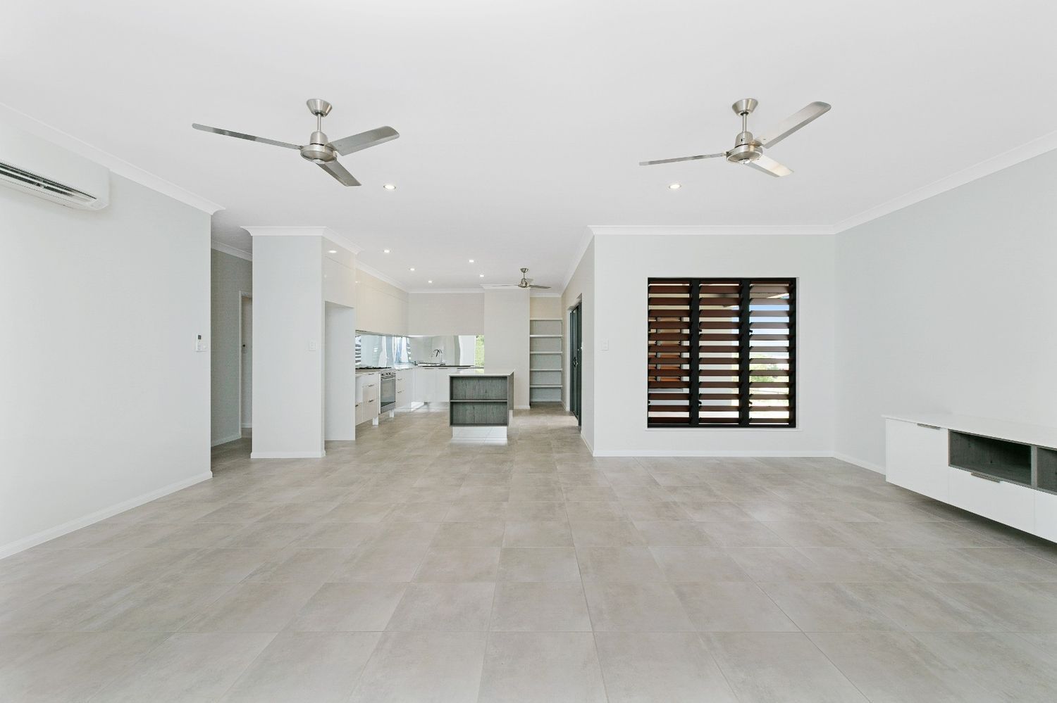 An Empty Living Room With Two Ceiling Fans and a Kitchen in the Background — Ashlee Jones Homes in Gordonvale, QLD