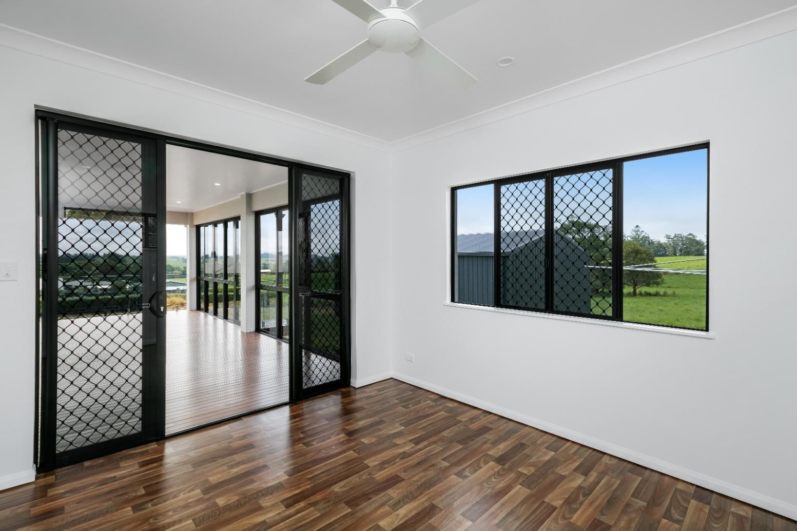 An Empty Room With Hardwood Floors and a Ceiling Fan — Ashlee Jones Homes in Gordonvale, QLD