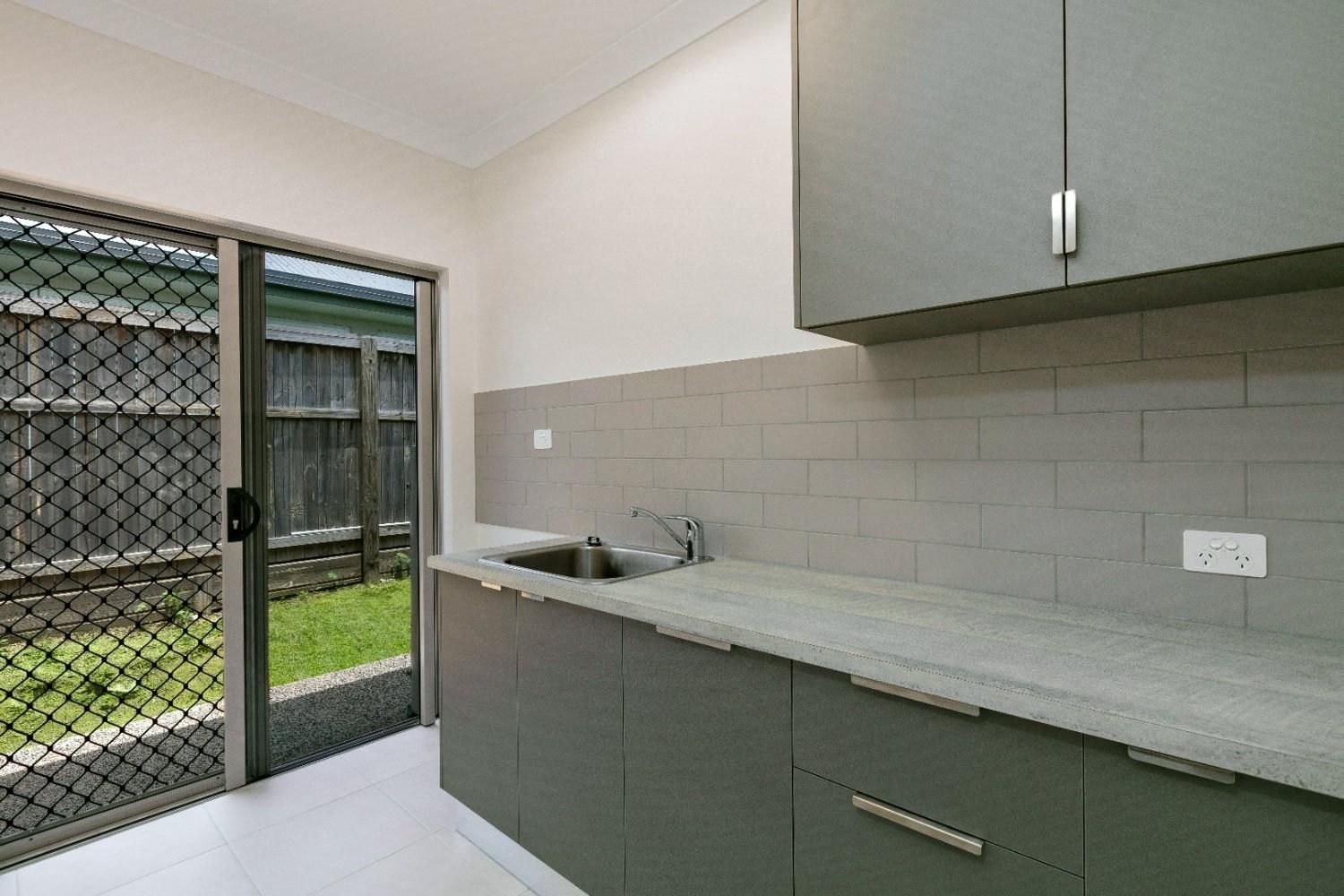 A Kitchen With a Sink and Cabinets and a Sliding Glass Door Leading to a Backyard — Ashlee Jones Homes in Gordonvale, QLD