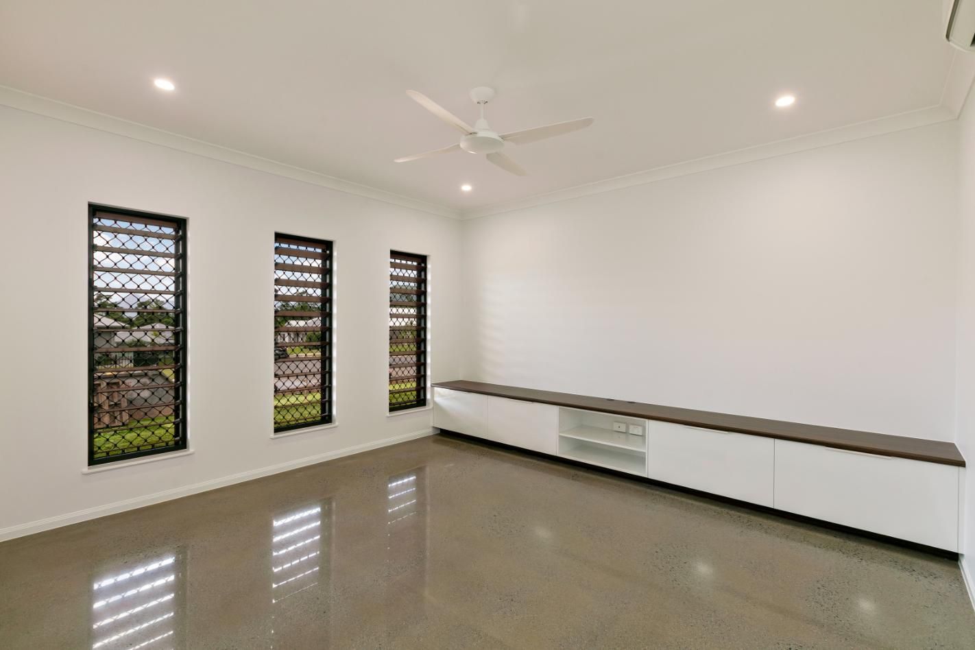 An Empty Living Room With a Ceiling Fan and Three Windows — Ashlee Jones Homes in Gordonvale, QLD