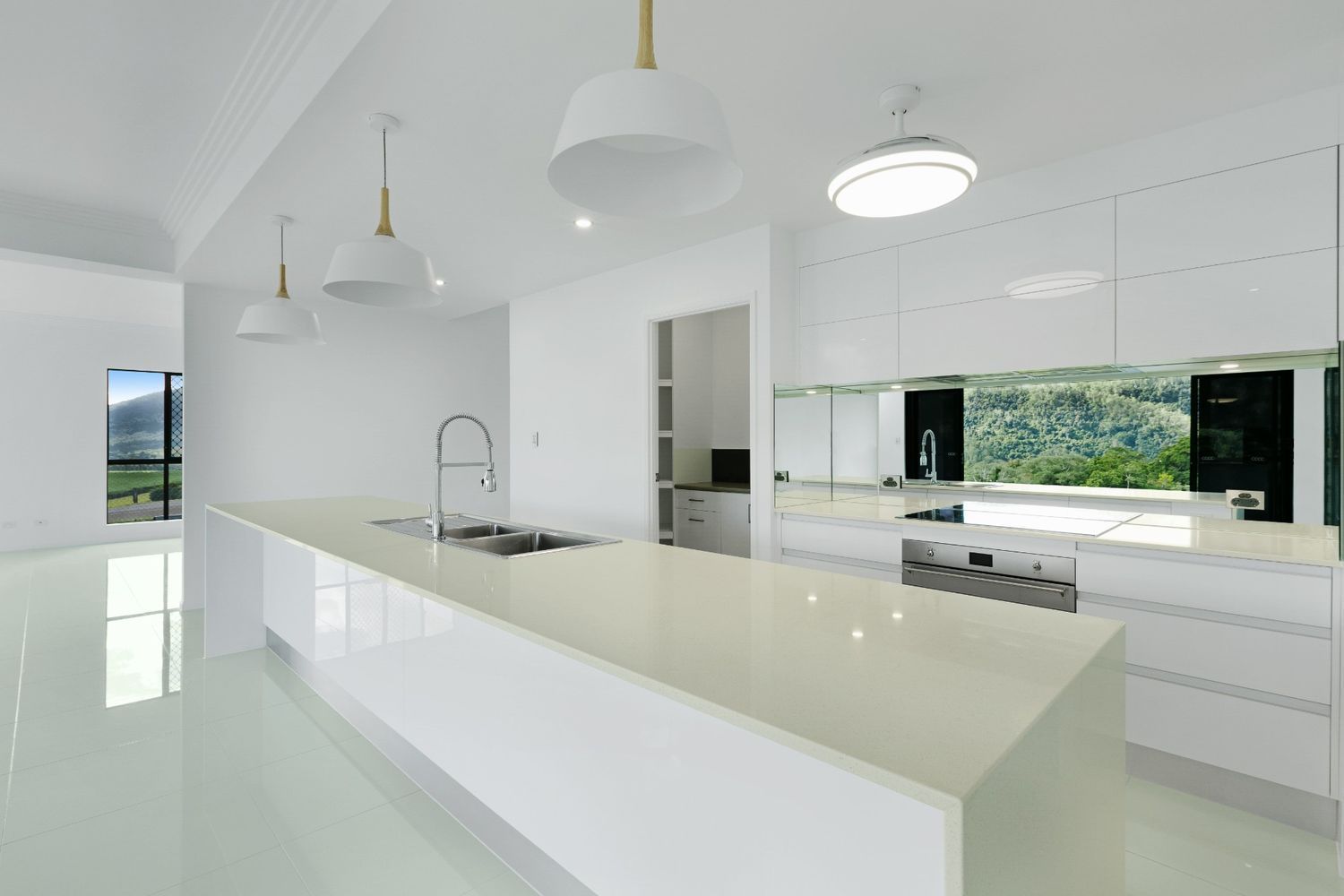 An Empty Kitchen With White Cabinets and Counter Tops and a Large Island — Ashlee Jones Homes in Gordonvale, QLD