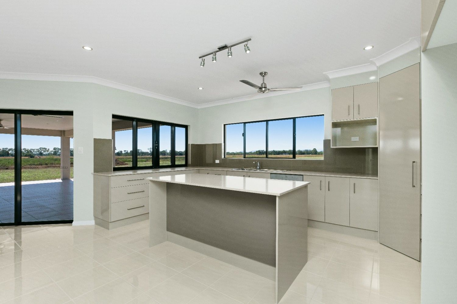 An Empty Kitchen With White Cabinets and a Large Island — Ashlee Jones Homes in Gordonvale, QLD