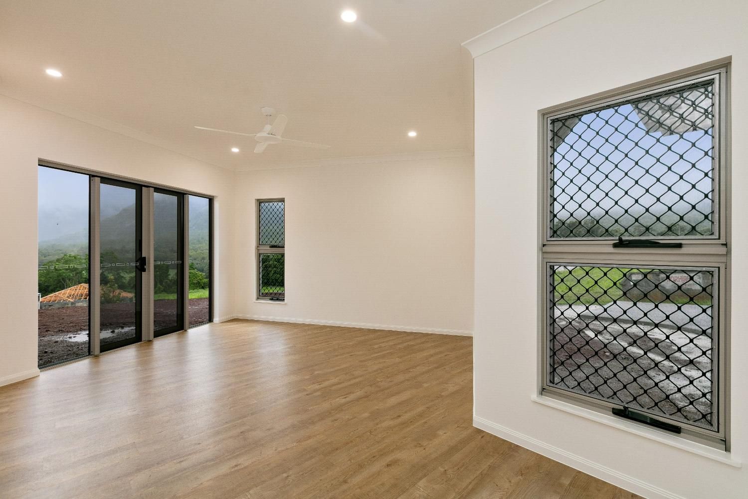An Empty Living Room With Sliding Glass Doors and Two Windows — Ashlee Jones Homes in Gordonvale, QLD