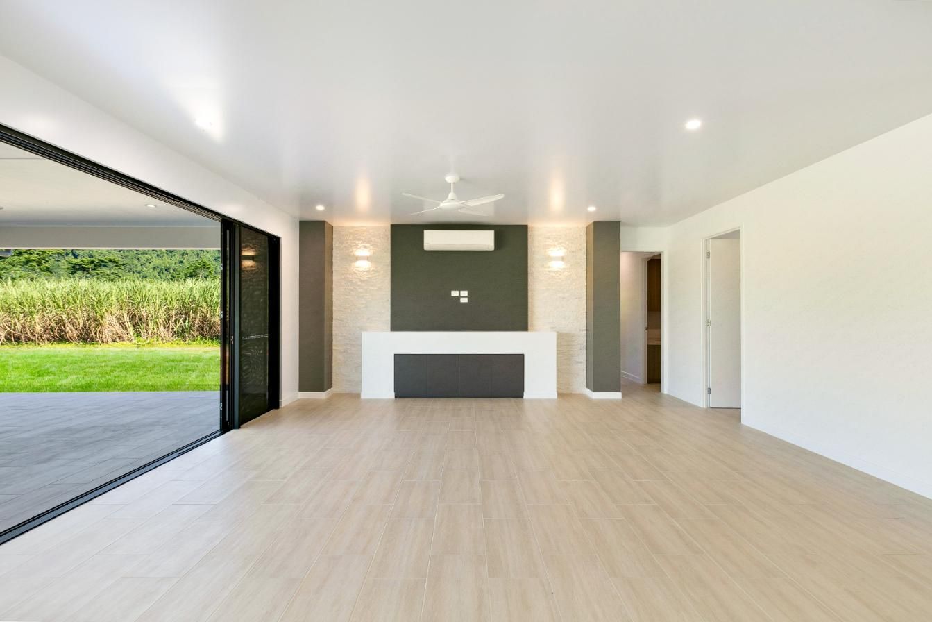 An Empty Living Room With Hardwood Floors and Sliding Glass Doors Leading to a Patio — Ashlee Jones Homes in Gordonvale, QLD