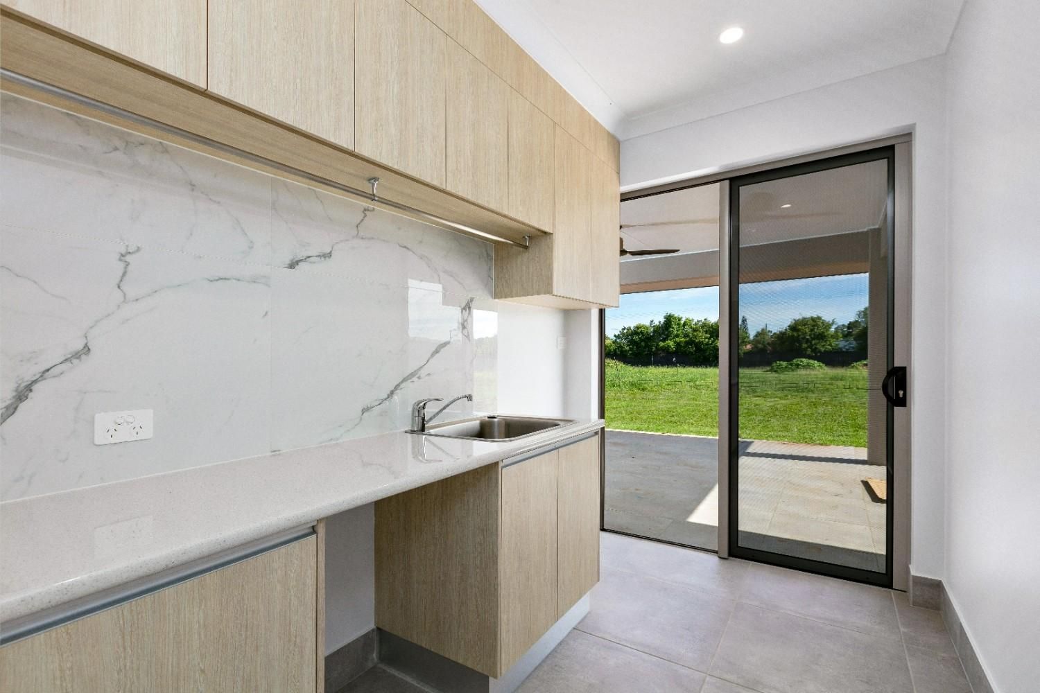 A Kitchen With Wooden Cabinets, a Sink, and a Sliding Glass Door — Ashlee Jones Homes in Gordonvale, QLD