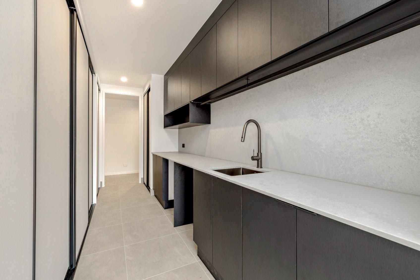 A Long Hallway with Black Cabinets and A Sink in A Kitchen — Ashlee Jones Homes in Gordonvale, QLD