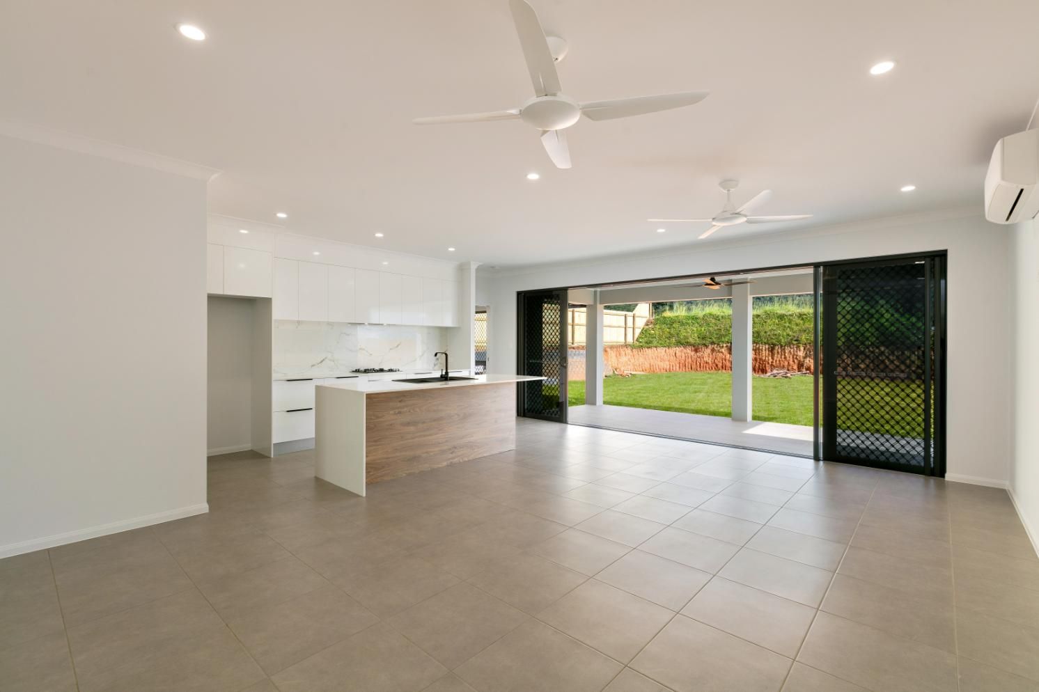 An Empty Living Room With a Kitchen and a Ceiling Fan — Ashlee Jones Homes in Gordonvale, QLD