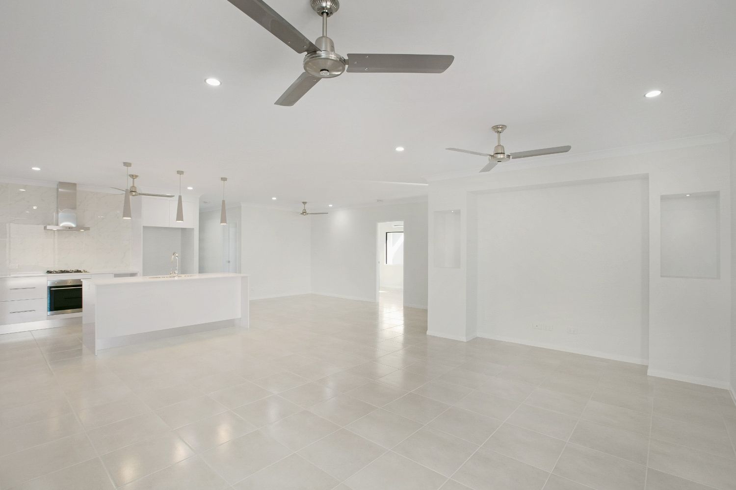 An Empty Room With a Ceiling Fan and a Kitchen in the Background — Ashlee Jones Homes in Gordonvale, QLD
