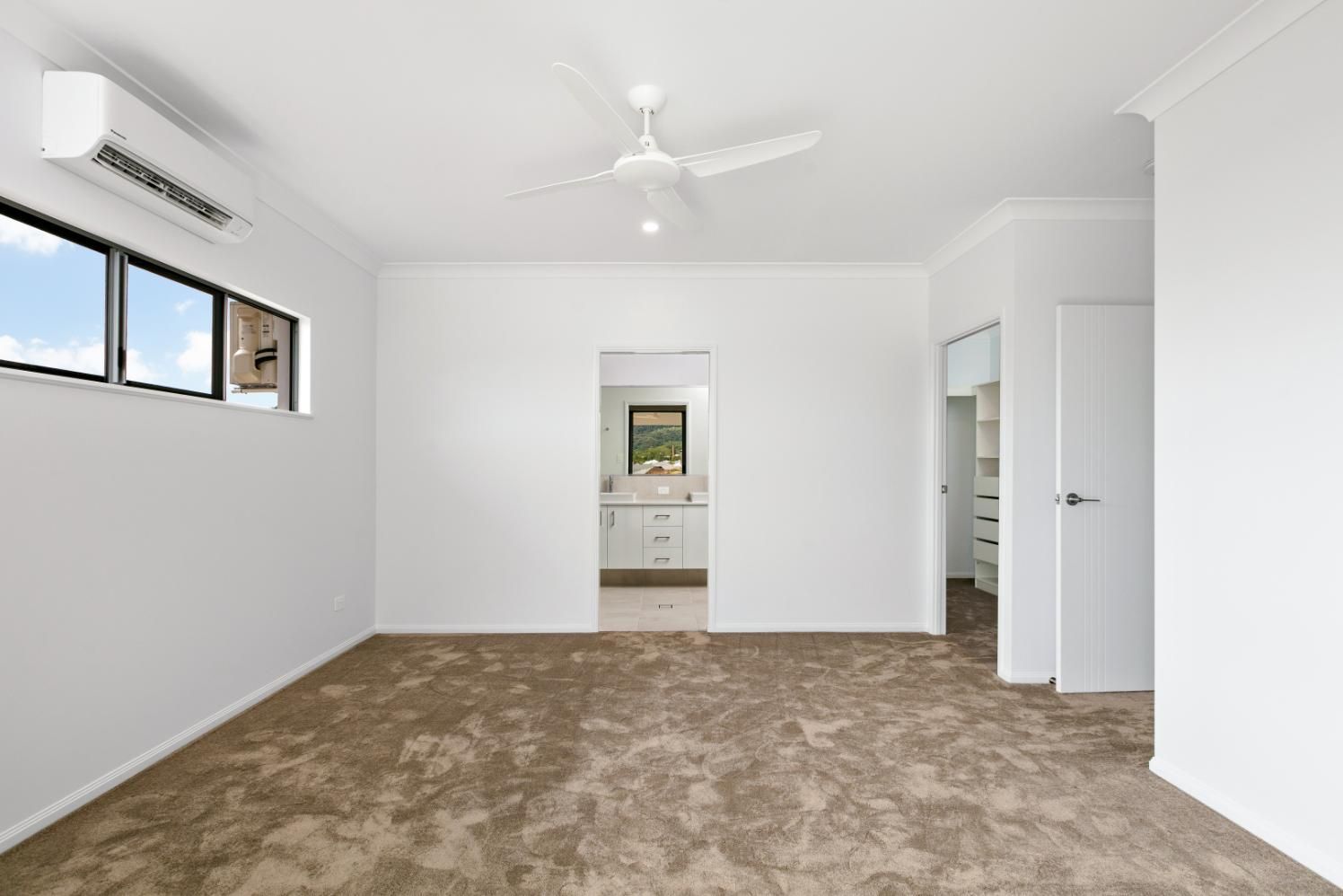 An Empty Bedroom With Brown Carpet and a Ceiling Fan — Ashlee Jones Homes in Gordonvale, QLD