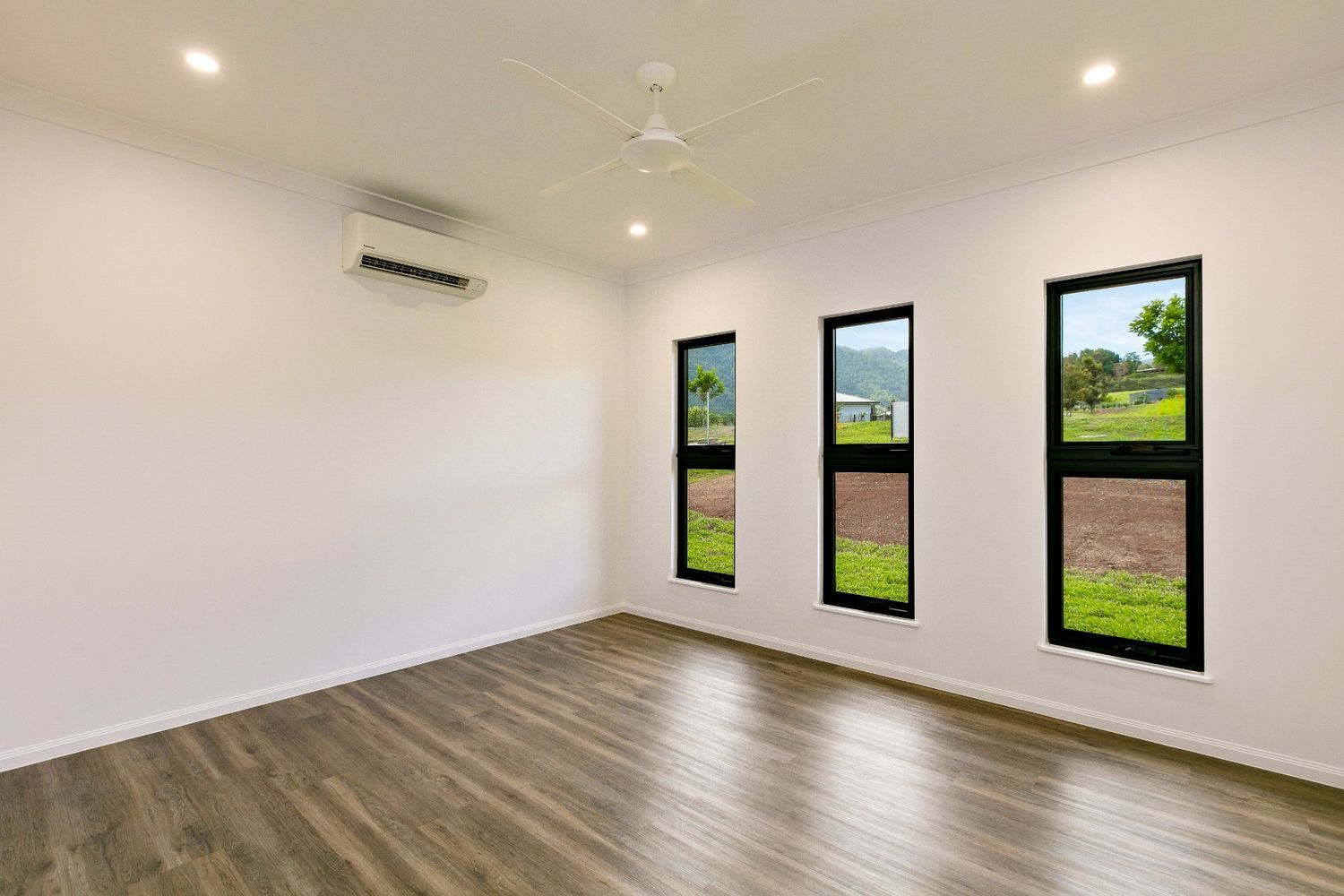 An Empty Room With Three Windows and a Ceiling Fan — Ashlee Jones Homes in Gordonvale, QLD