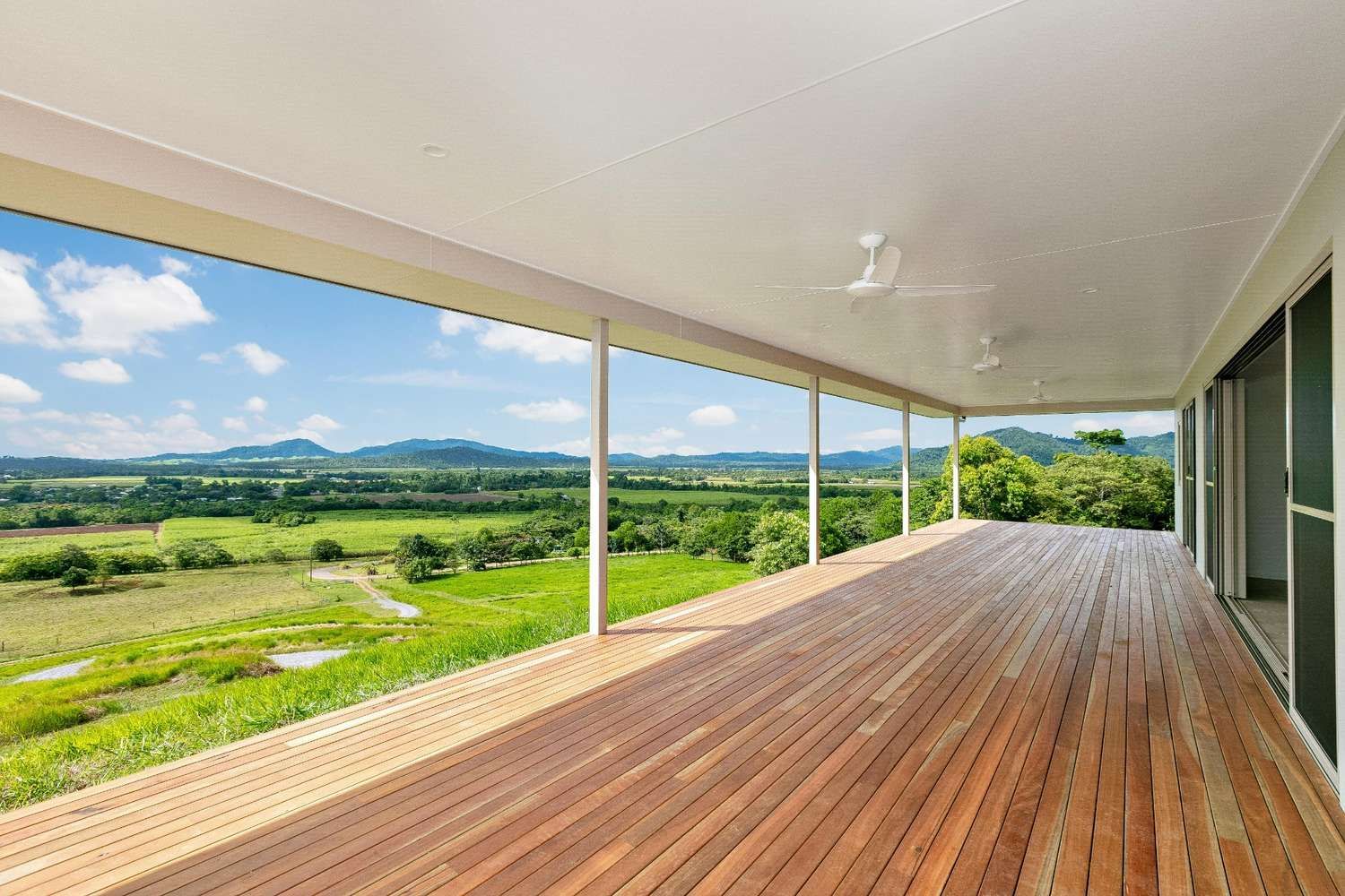 A Large Wooden Deck With a View of a Field and Mountains — Ashlee Jones Homes in Gordonvale, QLD