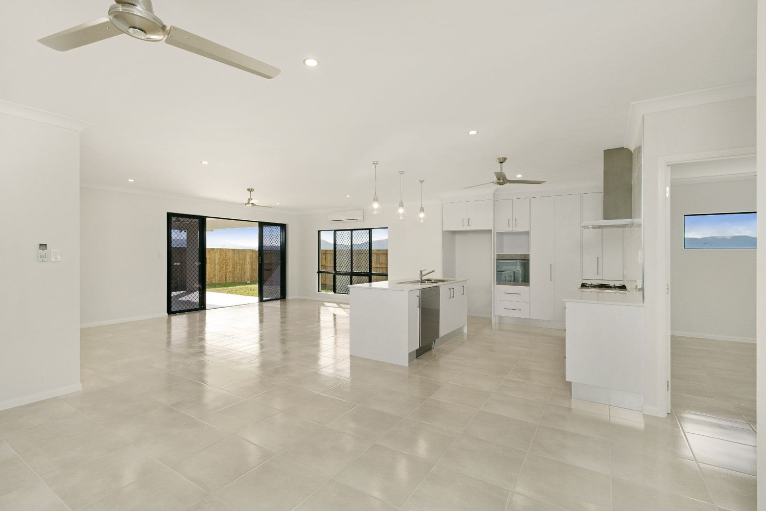 A Large Empty Room With a Ceiling Fan and a Kitchen — Ashlee Jones Homes in Gordonvale, QLD