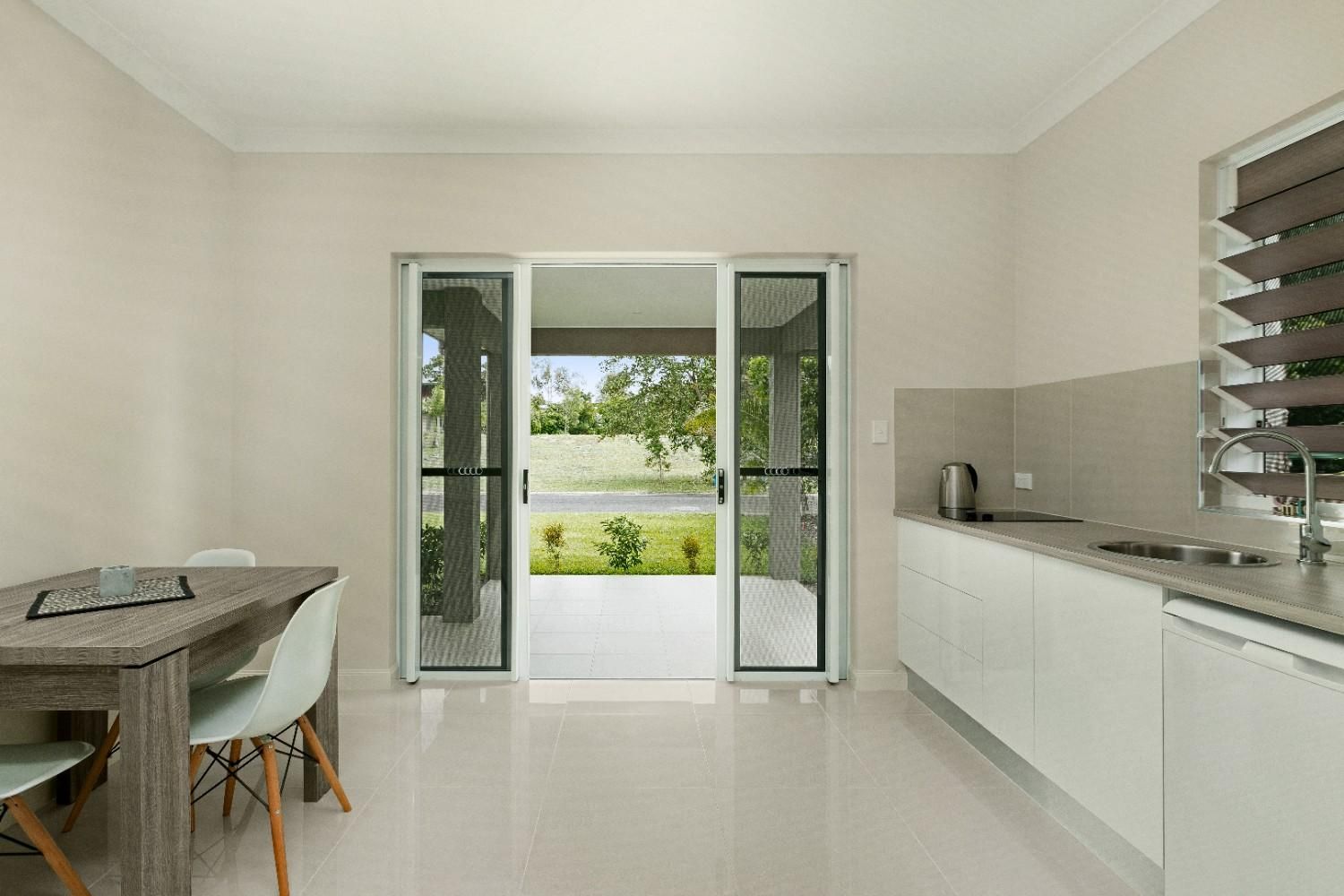 A Kitchen With a Table and Chairs and a Sliding Glass Door Leading to a Patio — Ashlee Jones Homes in Gordonvale, QLD
