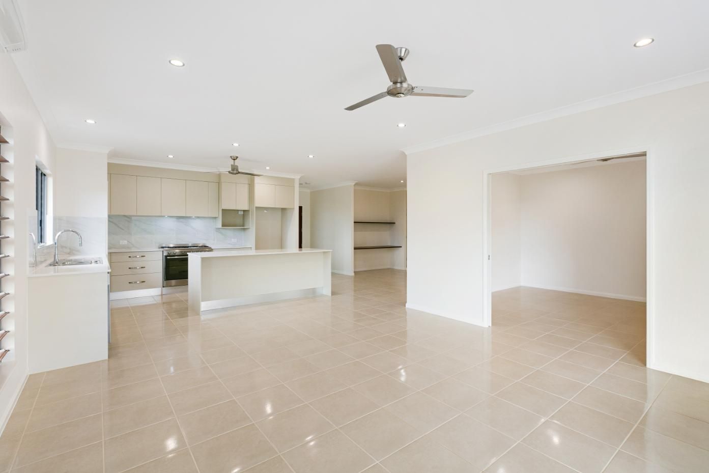 An Empty Room With a Ceiling Fan and a Kitchen in the Background — Ashlee Jones Homes in Gordonvale, QLD