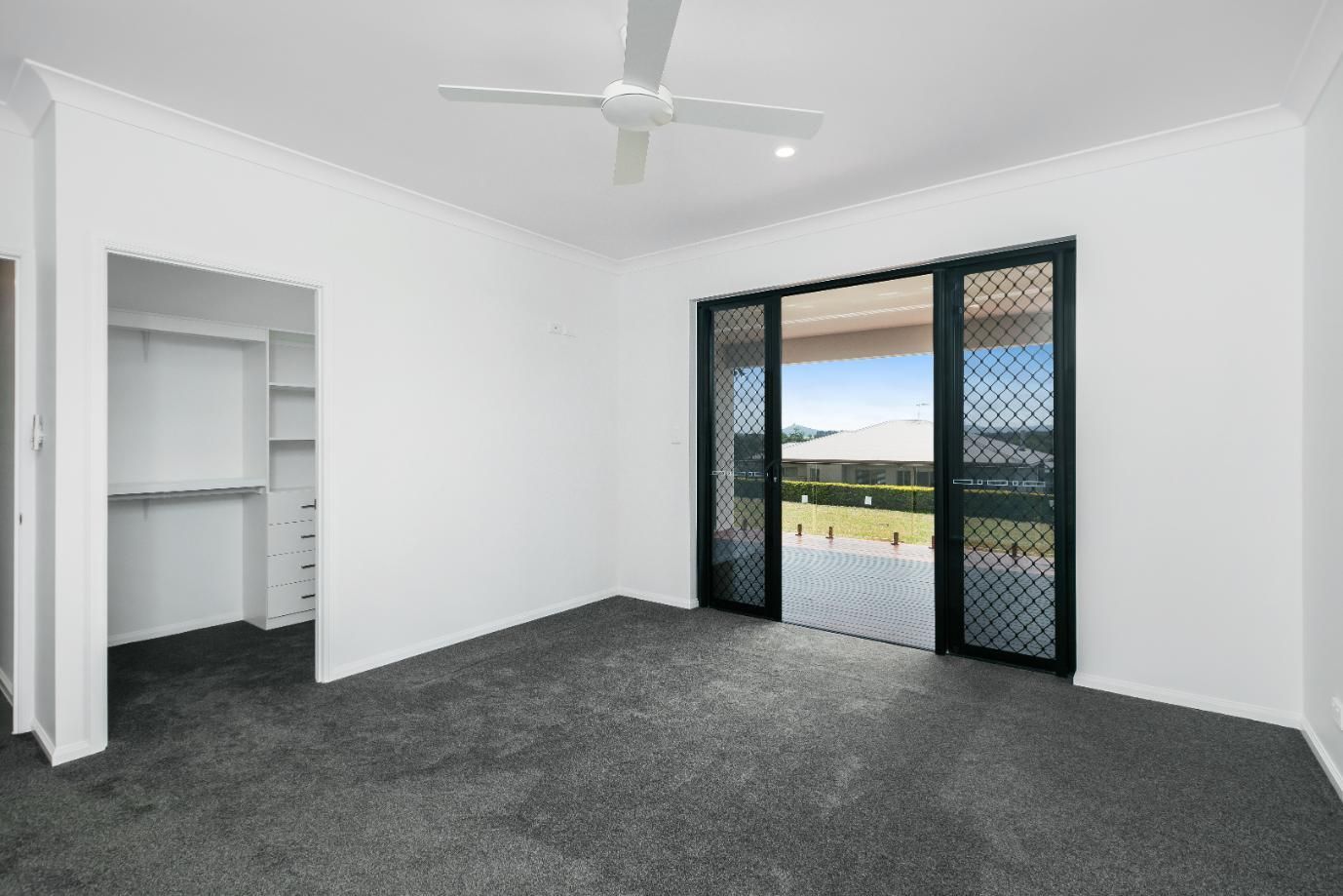 An Empty Bedroom With a Ceiling Fan and Sliding Glass Doors — Ashlee Jones Homes in Gordonvale, QLD