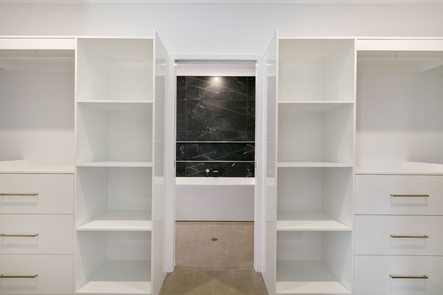 A Walk in Closet With Lots of Shelves and Drawers and a Bathroom in the Background — Ashlee Jones Homes in Gordonvale, QLD