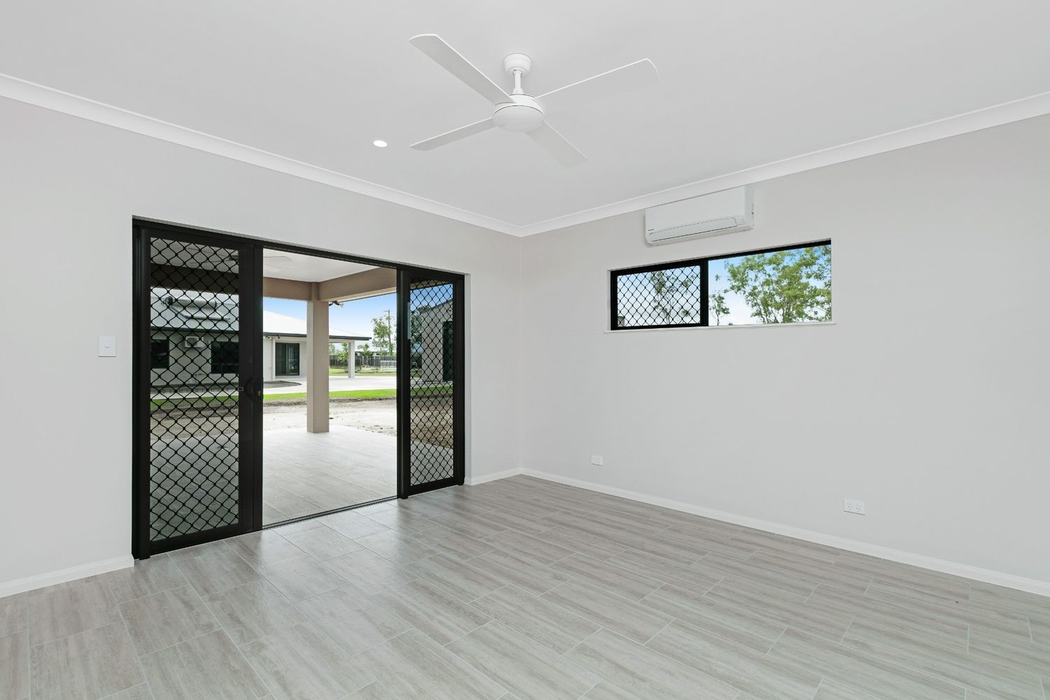 An Empty Living Room With a Ceiling Fan and Sliding Glass Doors Leading to a Patio — Ashlee Jones Homes in Gordonvale, QLD