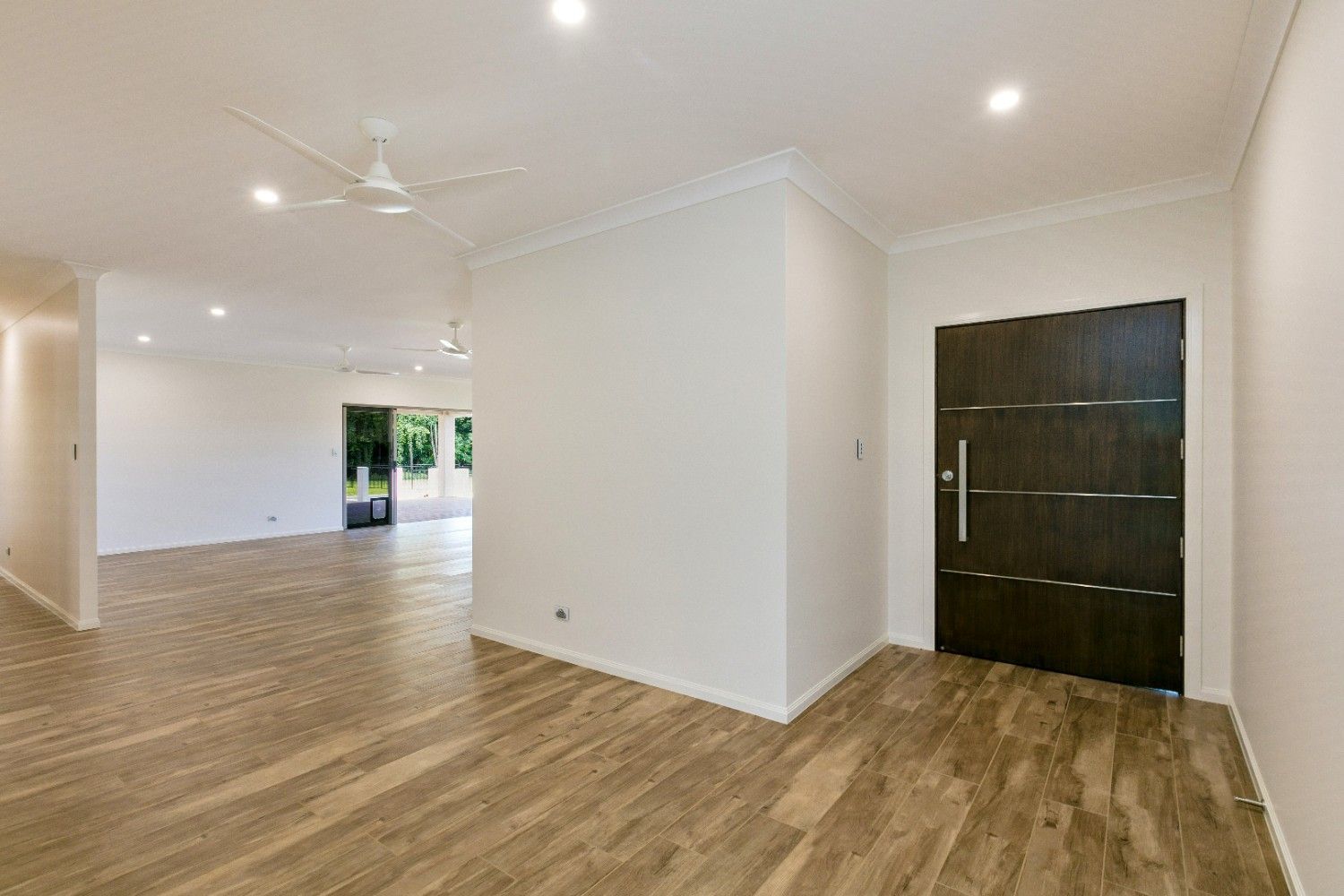 An Empty Living Room With Hardwood Floors and a Black Door — Ashlee Jones Homes in Gordonvale, QLD