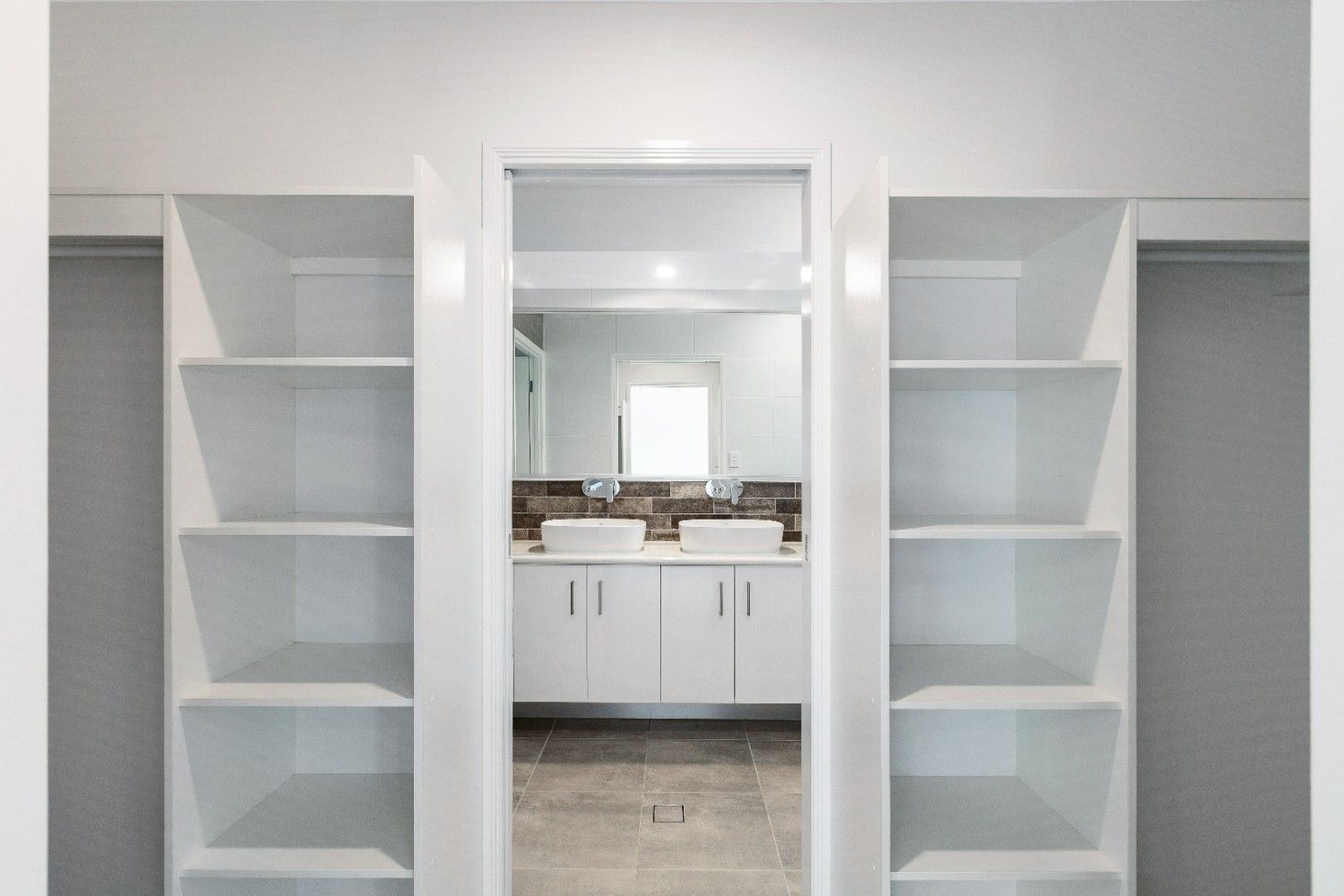 A Walk in Closet With Sliding Glass Doors Leading to a Bathroom With Two Sinks — Ashlee Jones Homes in Gordonvale, QLD