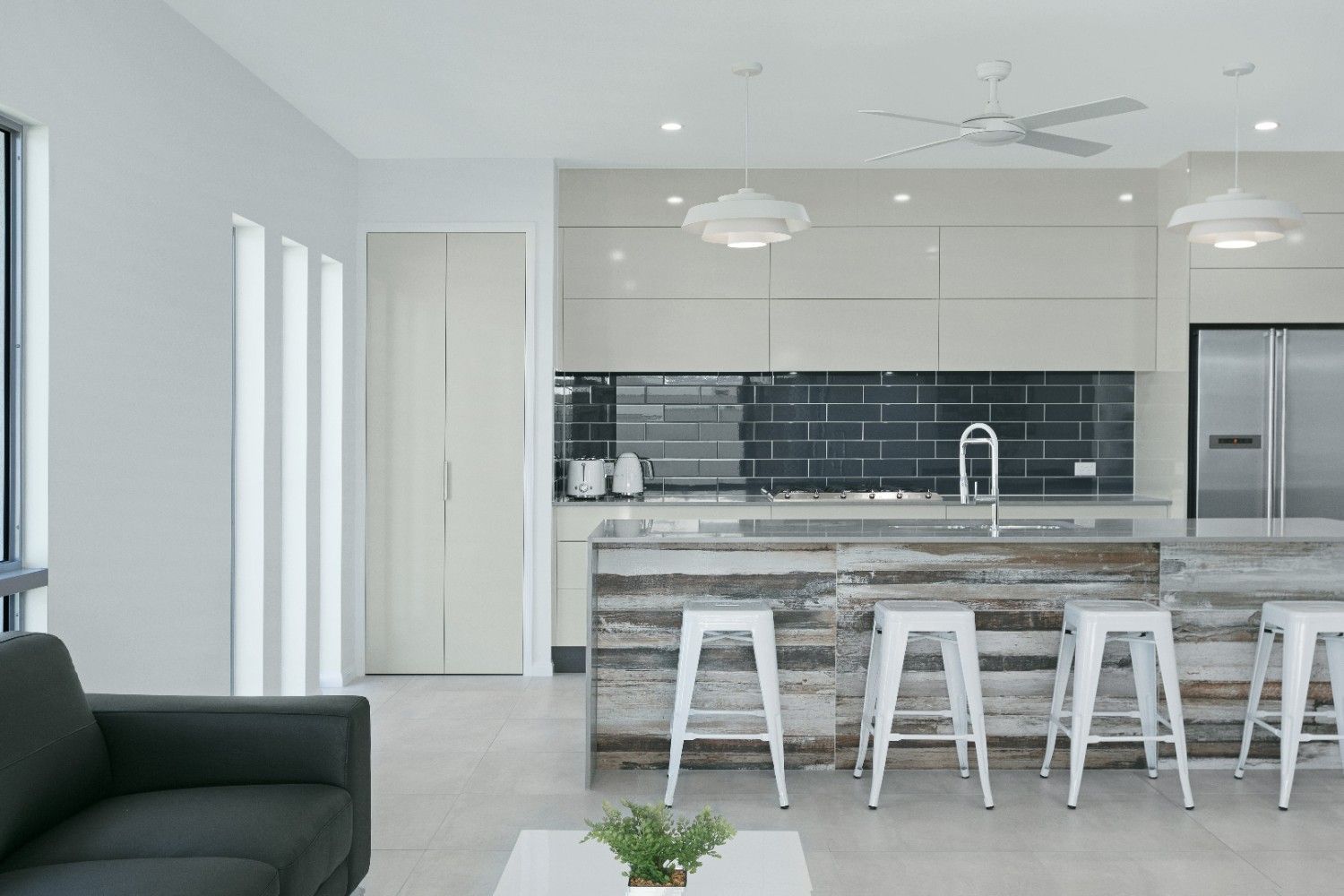 A Living Room With a Couch, Table, Stools and a Kitchen — Ashlee Jones Homes in Gordonvale, QLD