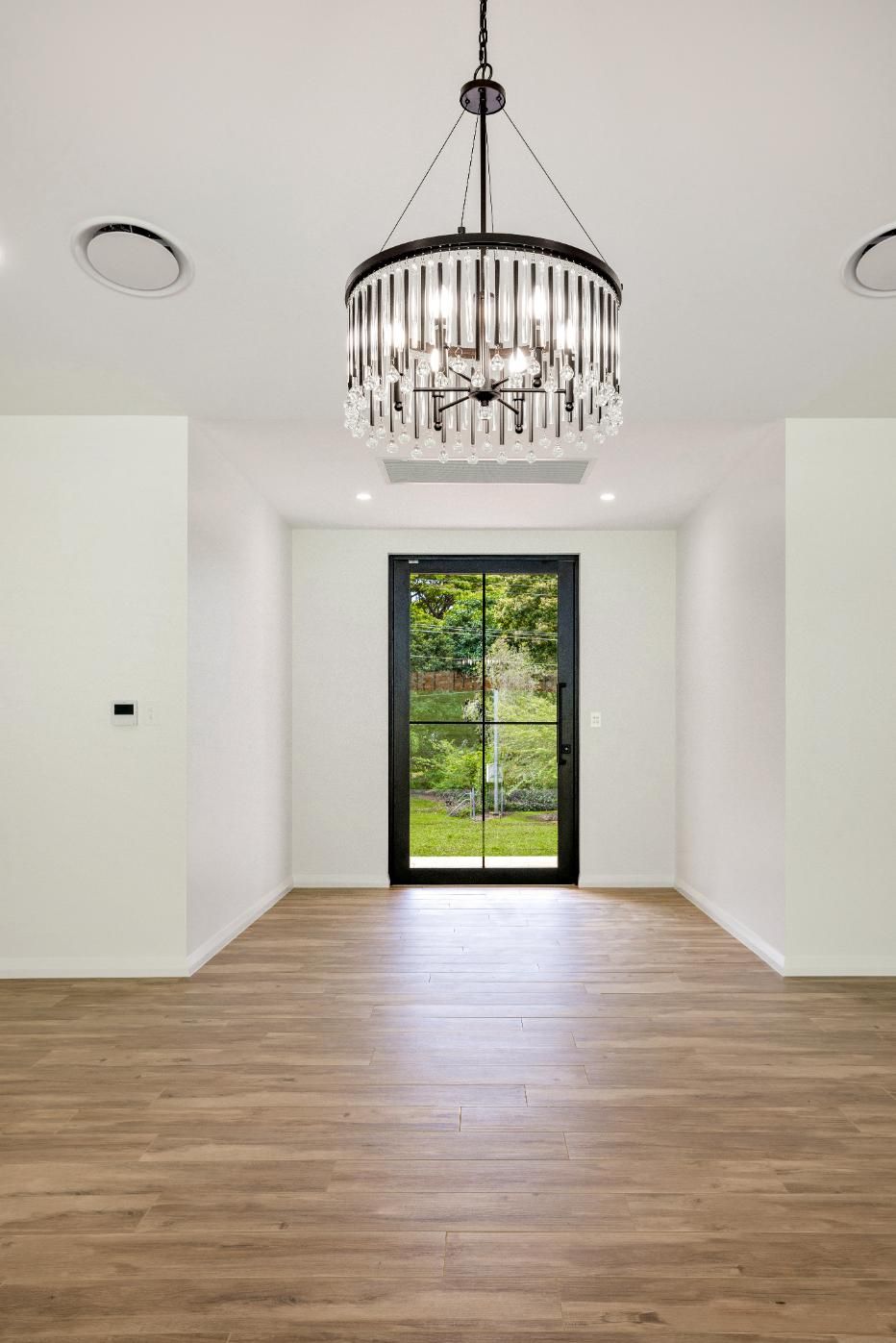 An Empty Room With Hardwood Floors and a Chandelier Hanging From the Ceiling — Ashlee Jones Homes in Gordonvale, QLD