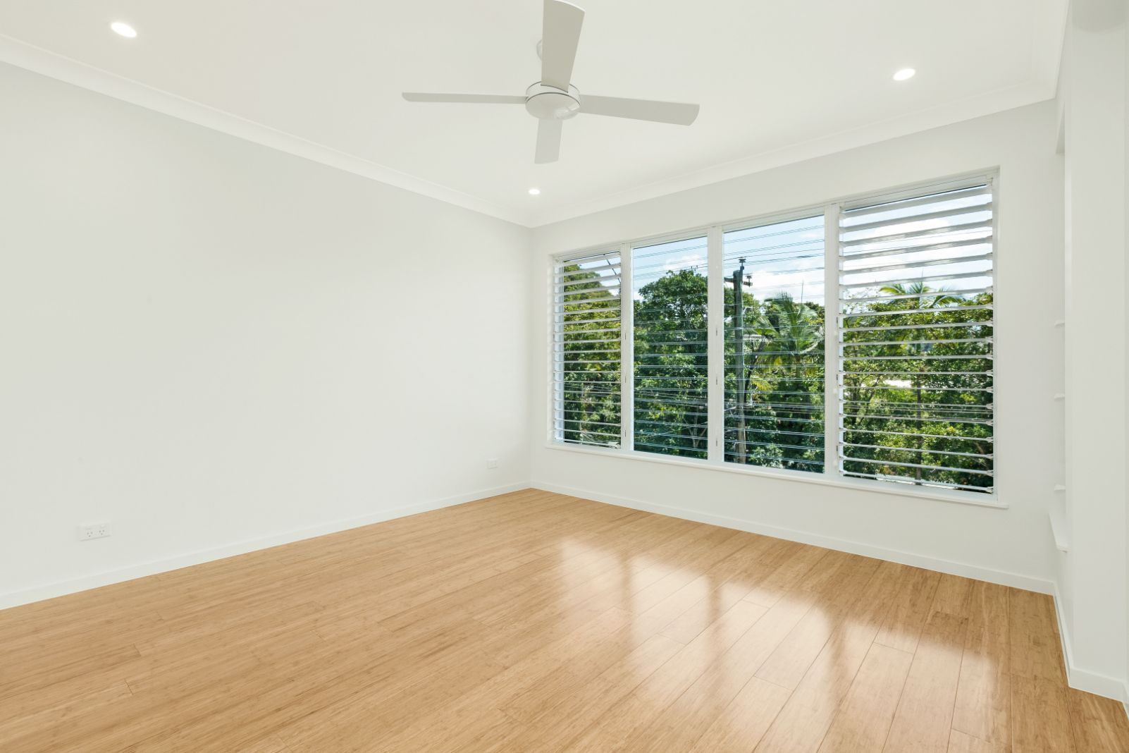 An Empty Room With Hardwood Floors and a Ceiling Fan — Ashlee Jones Homes in Gordonvale, QLD