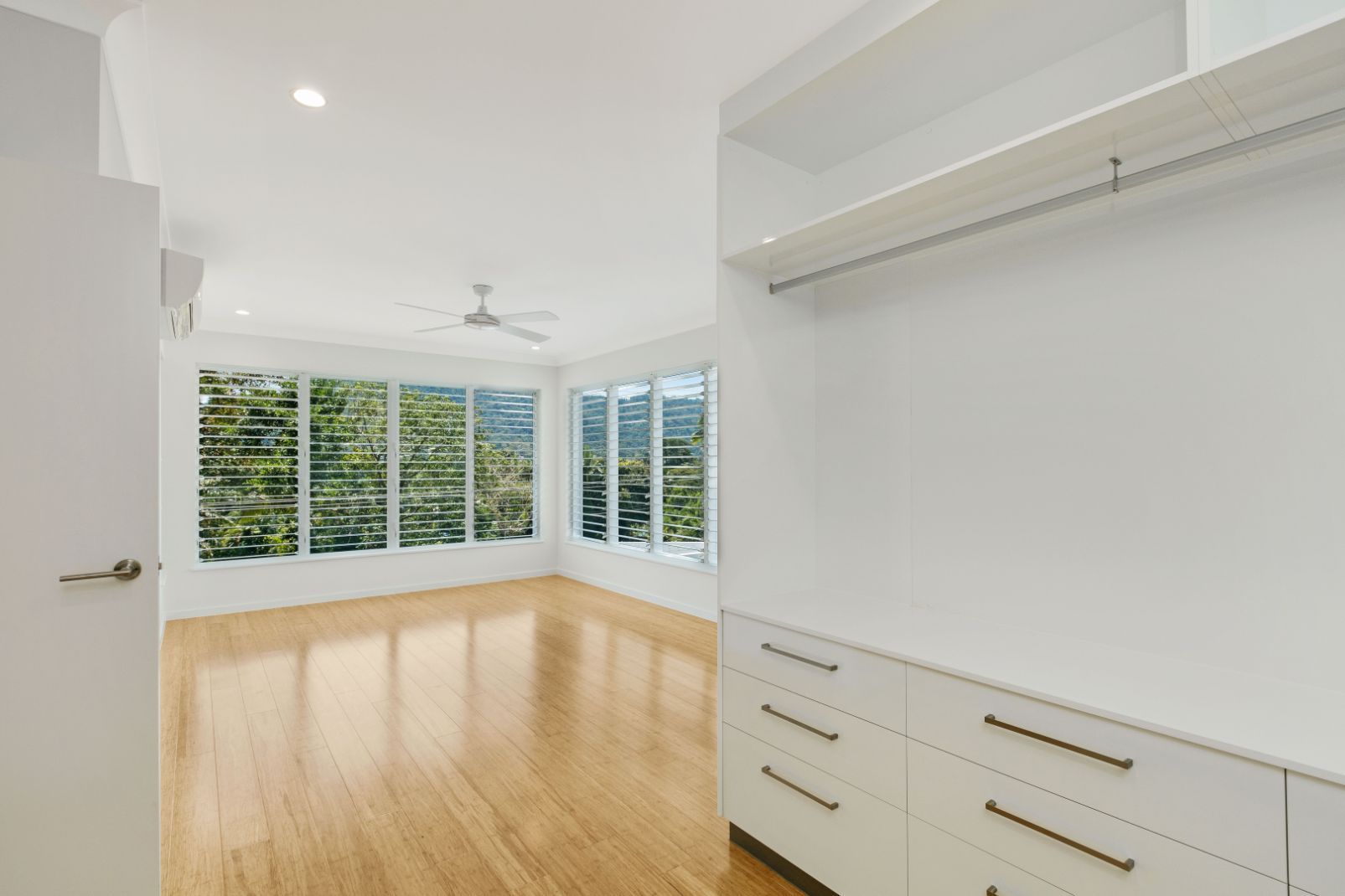 An Empty Room With Hardwood Floors, White Cabinets, and a Ceiling Fan — Ashlee Jones Homes in Gordonvale, QLD