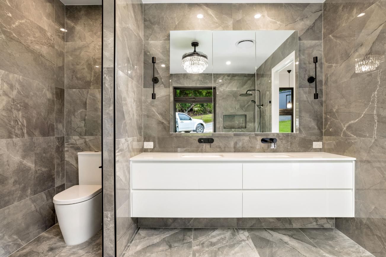 A Bathroom With a Toilet, Sink and Mirror — Ashlee Jones Homes in Gordonvale, QLD