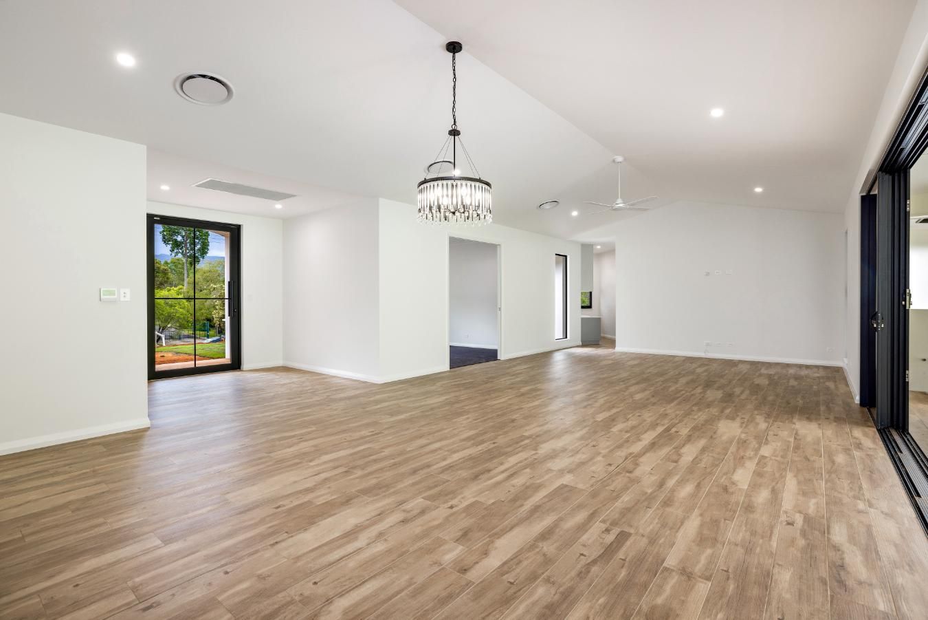 A Large Empty Room With Wooden Floors and White Walls — Ashlee Jones Homes in Gordonvale, QLD