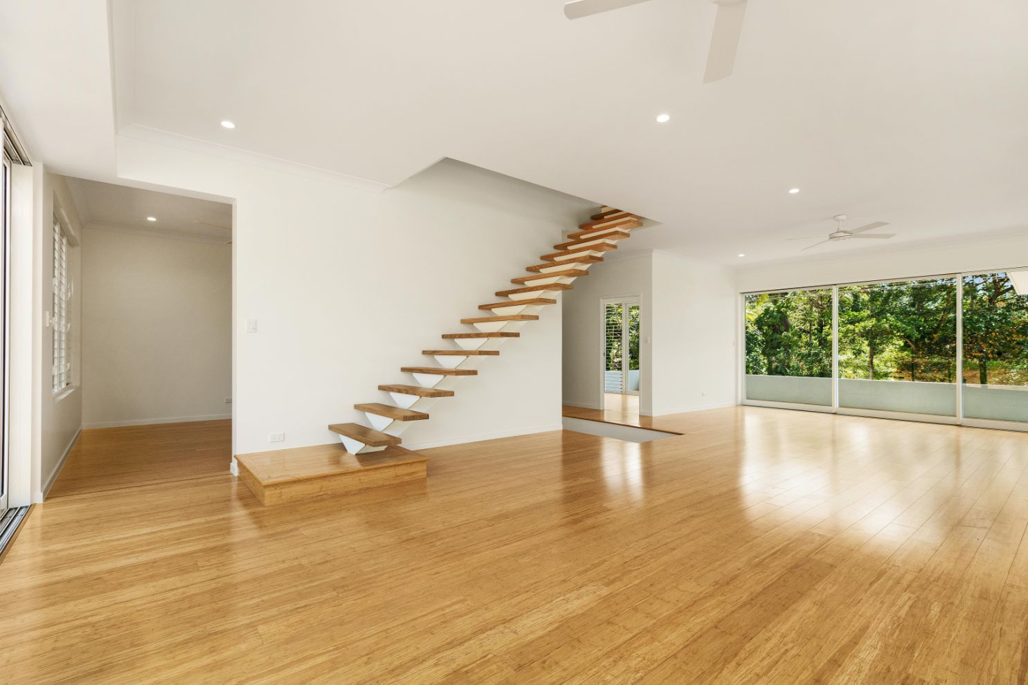 An Empty Living Room With Hardwood Floors and a Wooden Staircase — Ashlee Jones Homes in Gordonvale, QLD