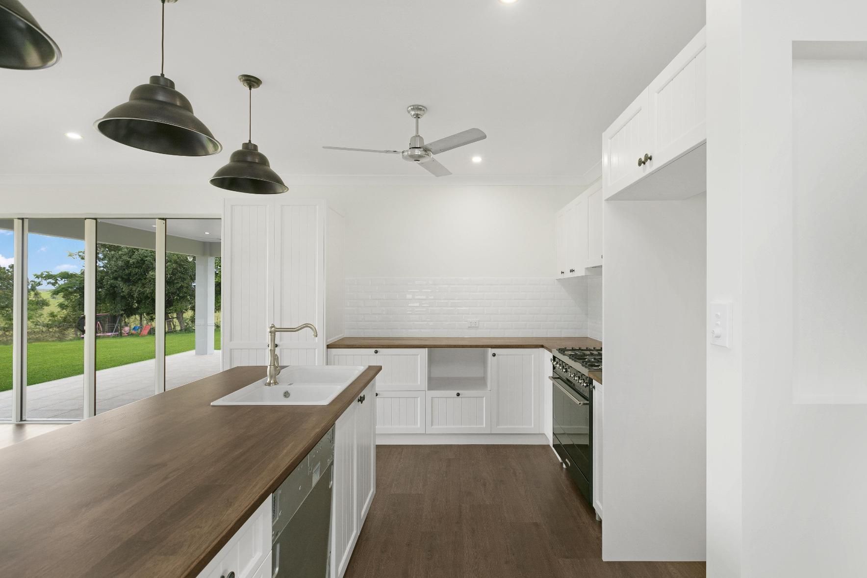 A Kitchen With White Cabinets and Wooden Counter Tops and a Ceiling Fan — Ashlee Jones Homes in Gordonvale, QLD