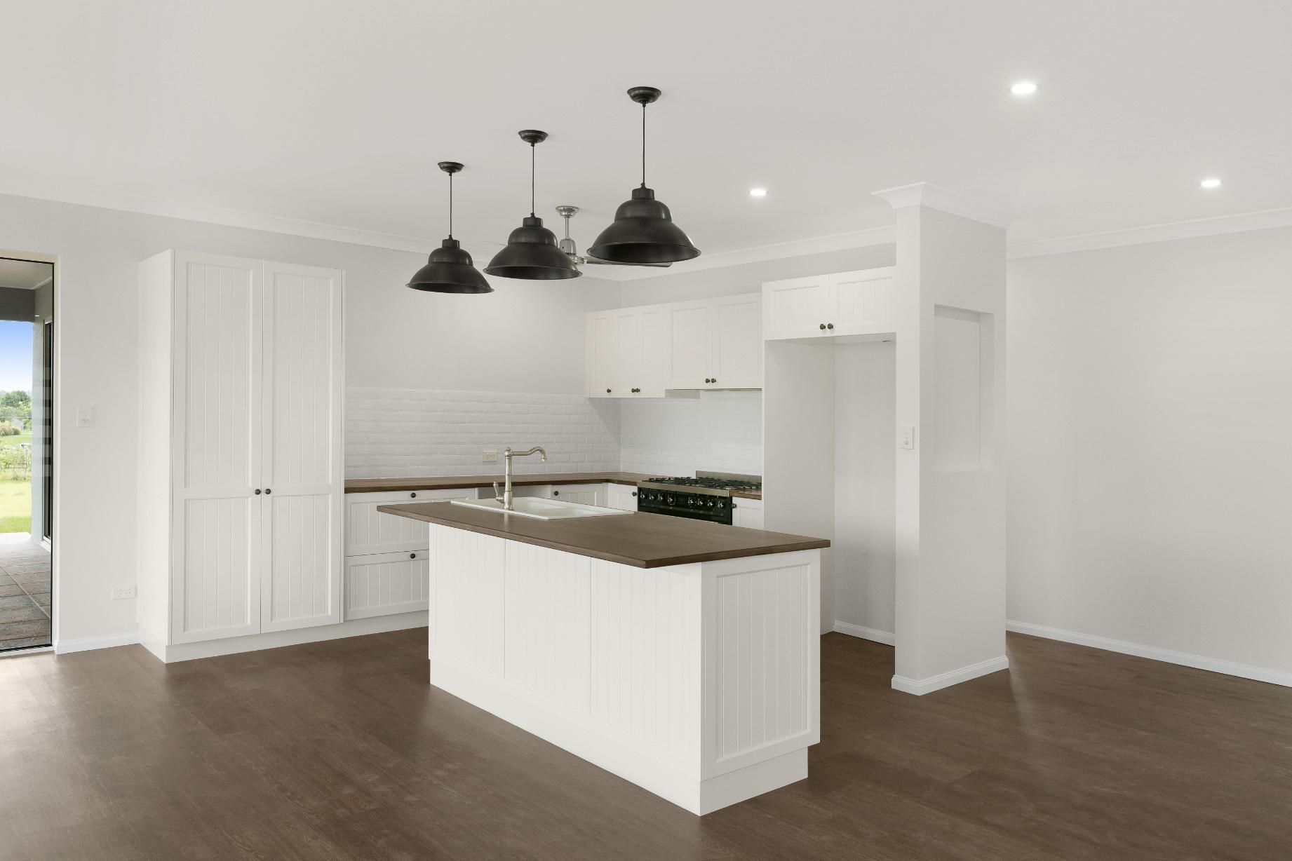 An Empty Kitchen With White Cabinets and a Large Island — Ashlee Jones Homes in Gordonvale, QLD